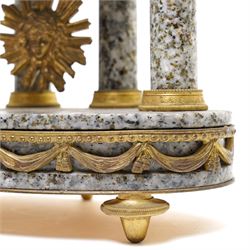 French- early 20th century portico clock garniture, 8-day drum movement decorated with laurel leaves to the glazed bezel and surmounted by a decorative urn with scroll handles, raised by four matching columns on a granite effect oval base with toupee feet, convex enamel dial with gilt pierced hands, Arabic numerals, minute markers and a garland of flowers, twin train Parisian rack striking movement, striking the hours and half hours on a bell. With a sunburst pendulum and key and a matching pair of two-light candelabra.
