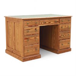 Contemporary stripped and waxed pine pedestal kneehole desk, rectangular top inset with green leather writing surface with brass studded edge, fitted with nine drawers with brass knob handles, above a plinth base on recessed castors