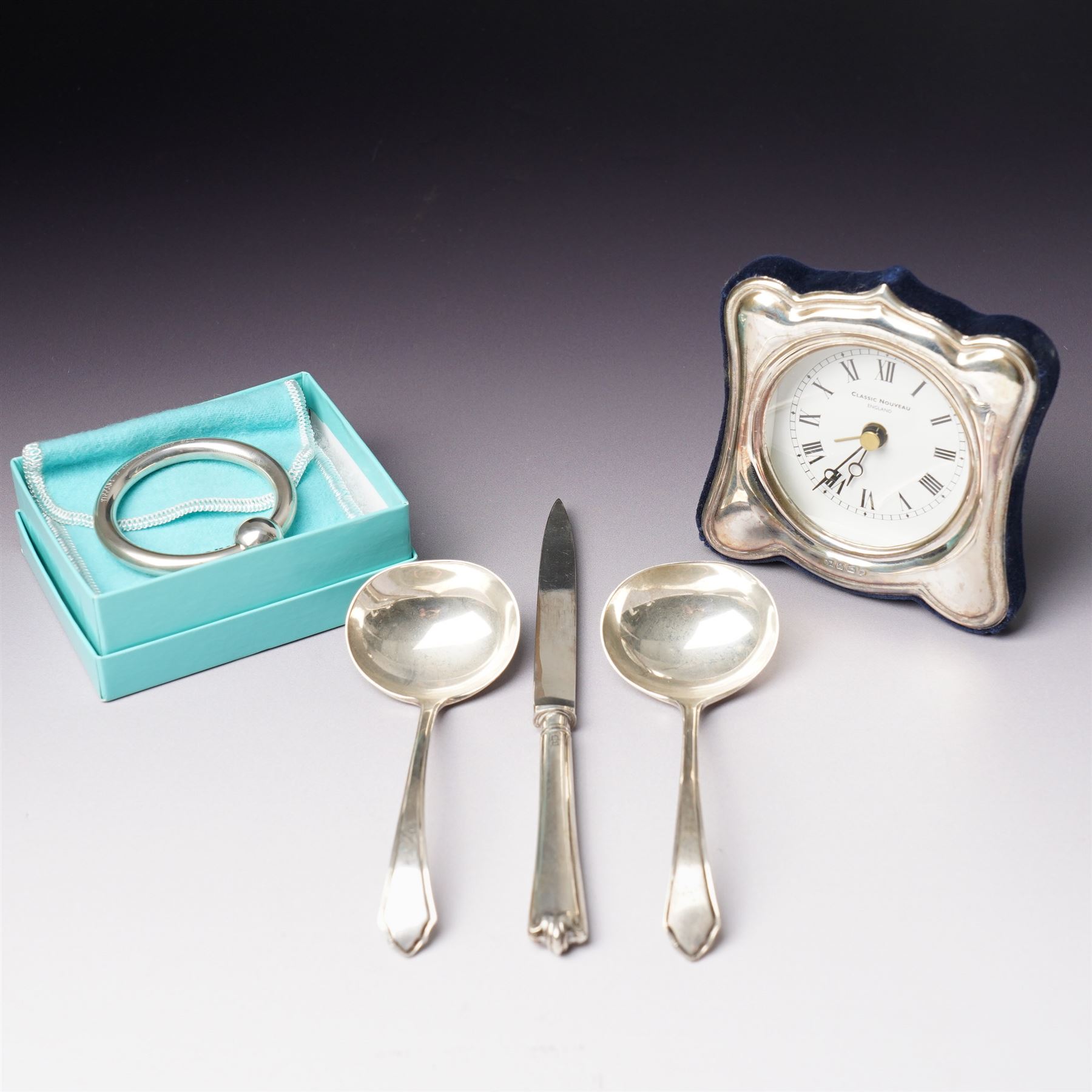 Tiffany silver teething ring marked 'Tiffany sterling 925', boxed, Junghans bedside clock in silver mounted frame, pair of silver sauce ladles and a silver knife