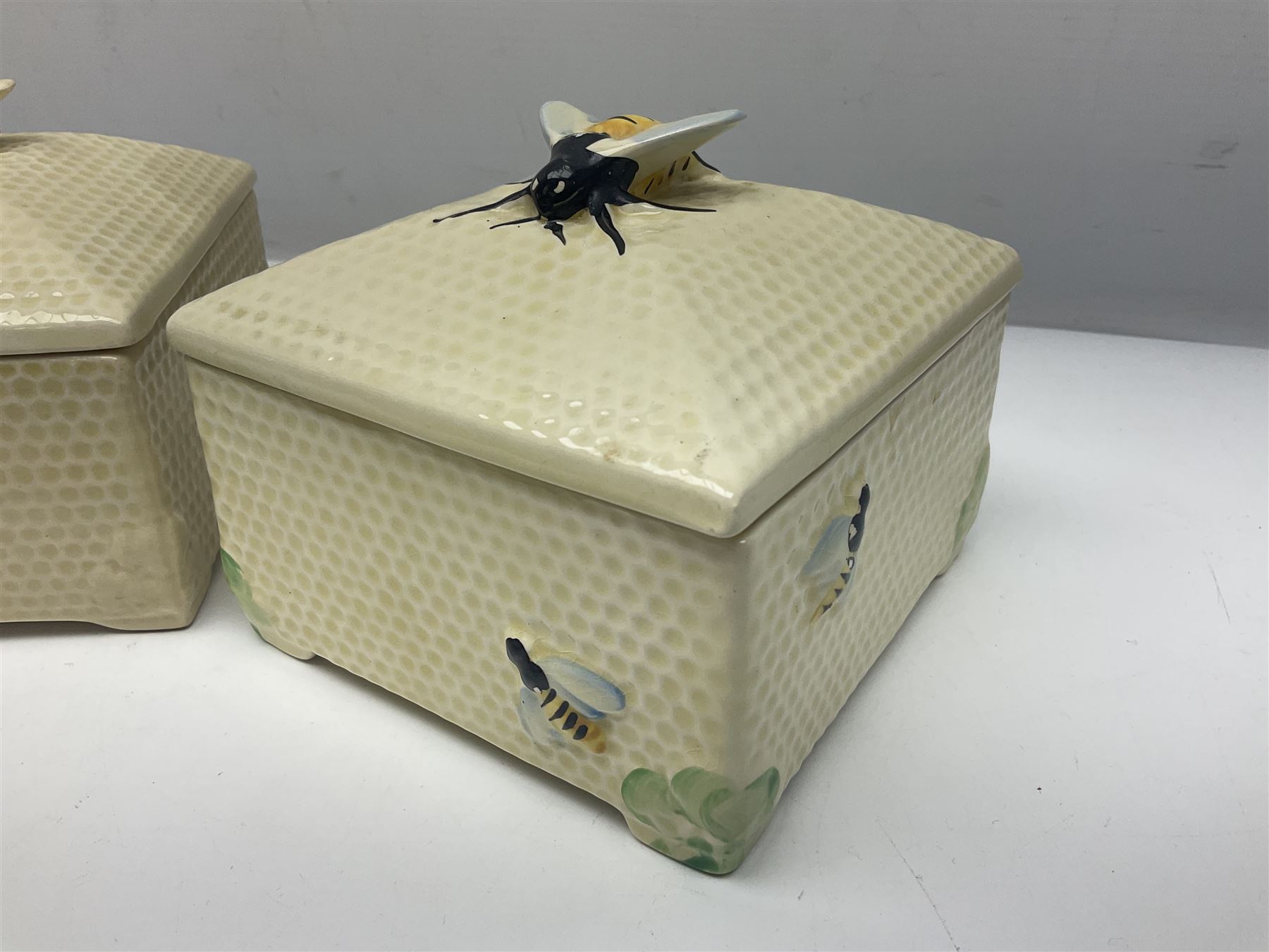 Four square honey boxes with lids,  each decorated with honeycomb pattern and finished with a bee finial