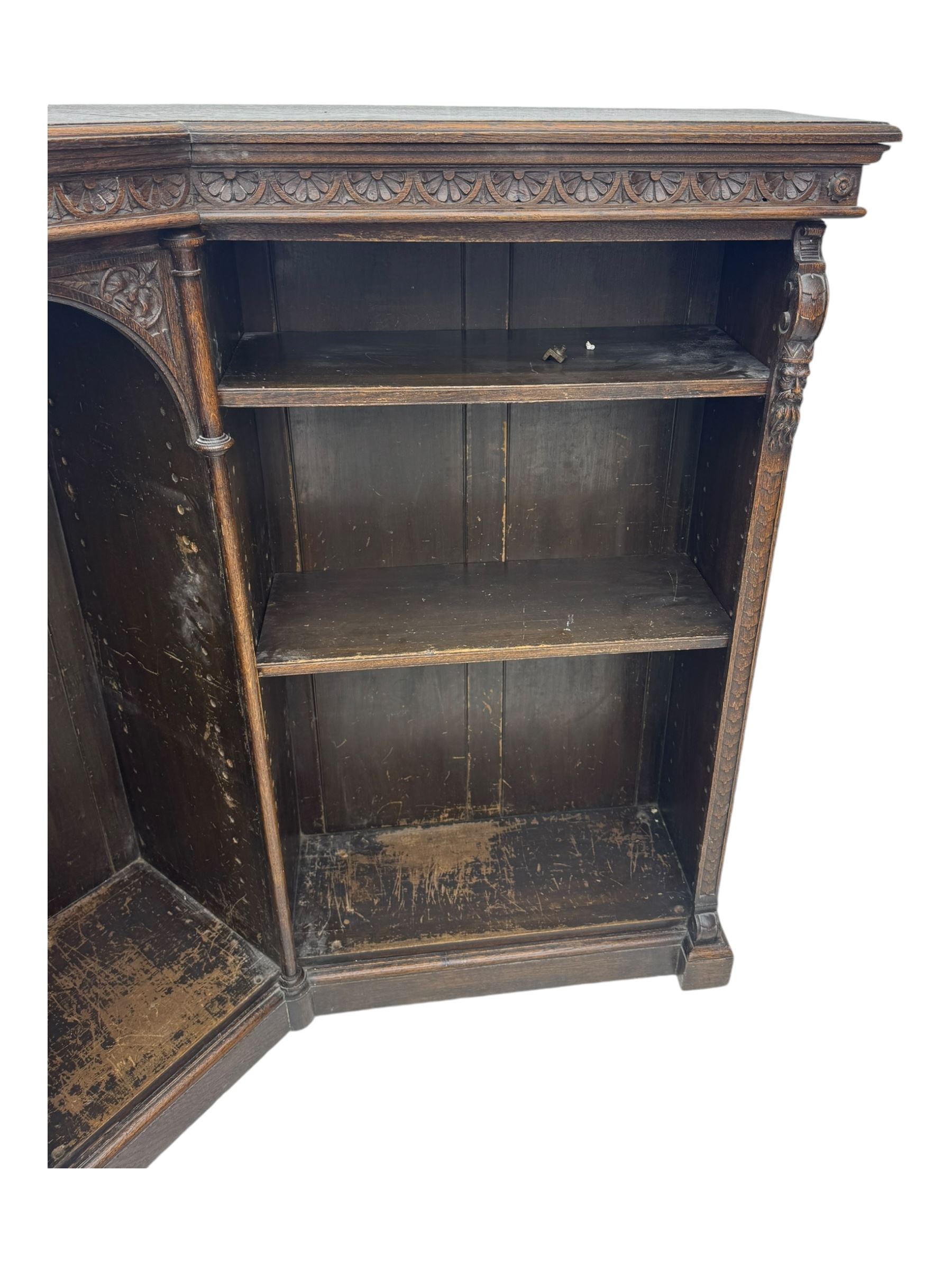 Victorian carved oak corner bookcase, L-shaped form, moulded top over lunette carved frieze, decorated with S-scroll and mask carved corbels with trailing acanthus leaves, fitted with adjustable shelves, on moulded plinth base 