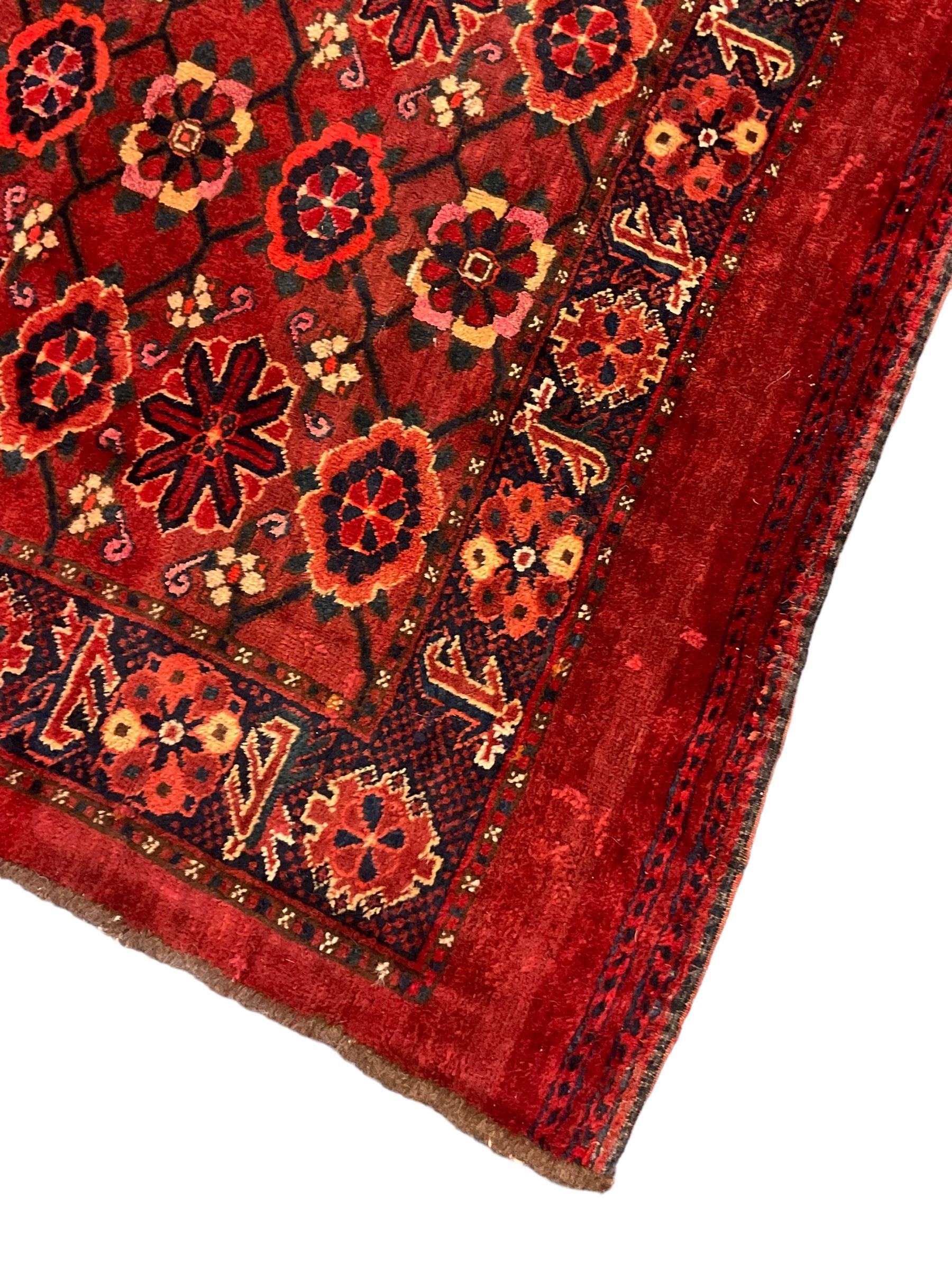 Persian red ground rug, the field decorated with lattice pattern and flowerhead, repeating border decorated with flower heads and leaf motifs