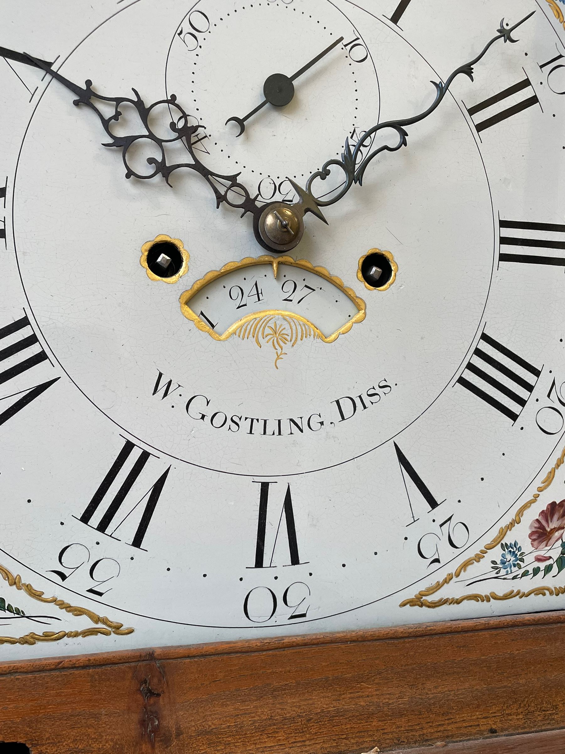 William Gostling of Diss  (Norfolk)-  Late 18th century 8-day oak longcase clock c1780-90, break arch top with scalloped cresting and three brass finials, glazed break arch hood door flanked by turned pilasters with brass capitals, trunk with a long trunk door and rounded top on a square plinth with an applied and shaped skirting, early painted Wilson of Birmingham dial with Roman numerals and five minute Arabic's, matching steel hands and second pointer, arched square ended calendar aperture with date disc behind, floral spandrels within gesso borders and a painted rocking automaton representing Mercury to the break arch, dial pinned via a false plate to a weight driven rack striking movement with a recoil anchor escapement, striking the hours on a cast bell. With pendulum weights and key. 
William Gostling (II) is recorded as working in Diss from 1774 to 1797, succeeded by widow Anne and son George . The dial of this clock is illustrated and discussed in detail in M.F. Tennants book 