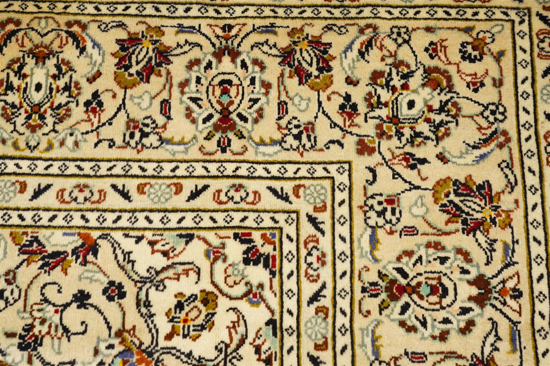 Central Persian Kashan hand-knotted carpet, ivory field with central lobed medallion issuing an all-over design of scrolling vines, palmettes, and floral sprays, within conforming spandrels, enclosed by a foliate border, framed by multiped guard stripes, with cotton fringe ends 