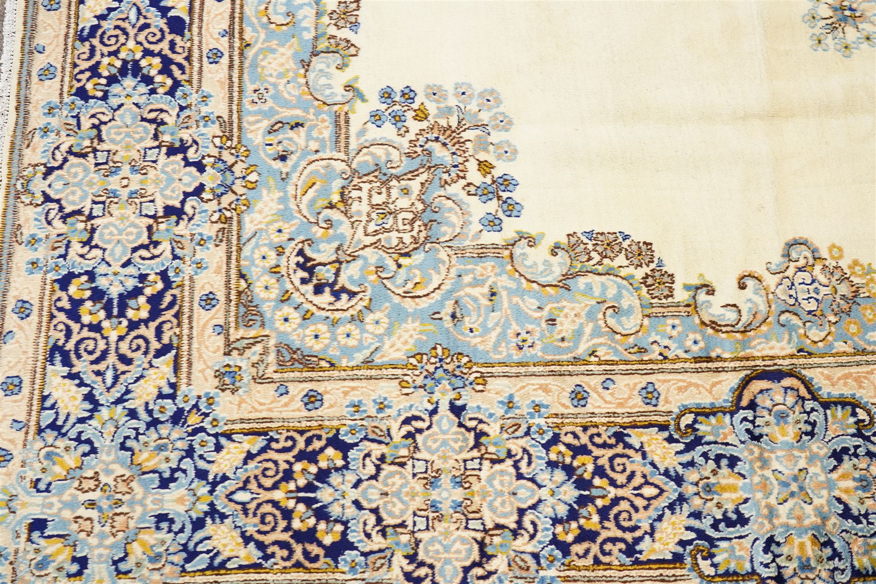 South East Persian Kirman hand-knotted carpet, ivory field with central floral medallion in tones of cobalt and pale blue, issuing scrolling vinery and palmettes, conforming spandrels, main border with scrolling foliage and stylized palmettes, framed by multiple guard borders, with cotton fringe ends 