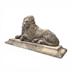 Neoclassical design cast stone garden lion, modelled recumbent with raised and flowing mane, on rectangular plinth base, with flat plain reverse, in weathered finish