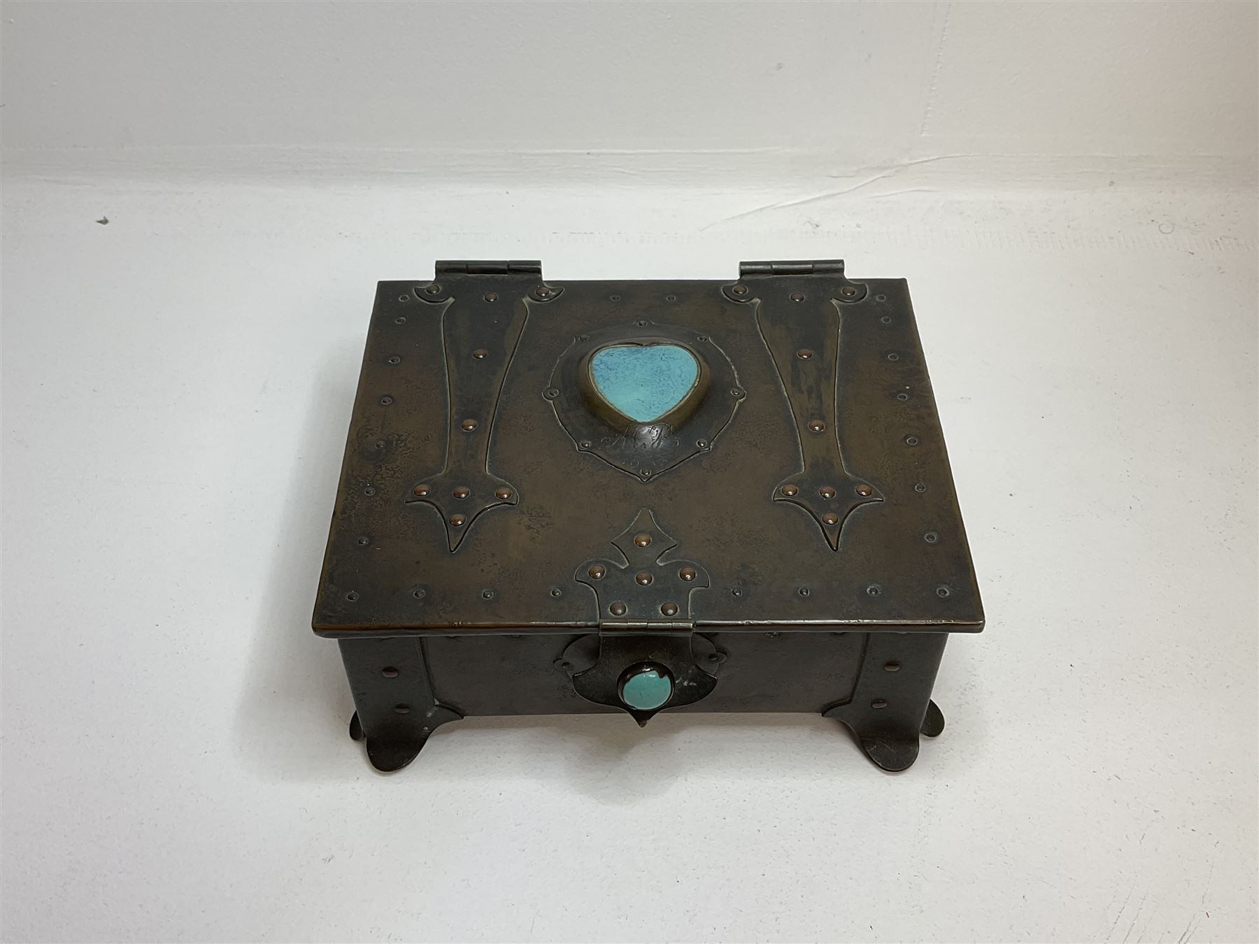 Arts and Crafts copper box, the lid decorated with stylised riveted hinges and inset with Ruskin type ceramic turquoise heart-shaped cabochon, the mount etched M.B 1913, and further cabochon roundel to each side panel, including one inset to the clasp acting as the knob to the locking mechanism, marked RS Douglas 1913 beneath, W16.5cm H7cm D15cm