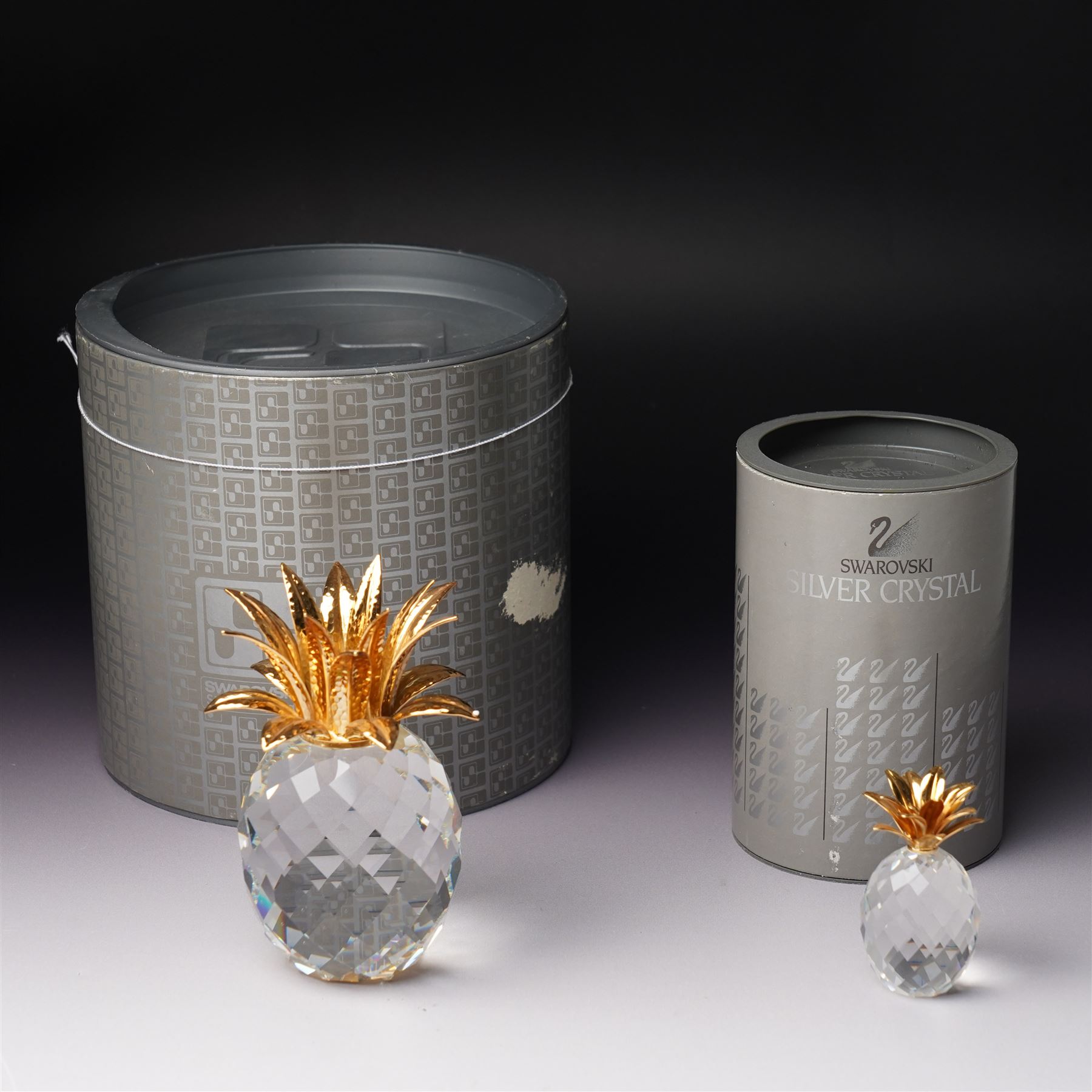 Pair of Swarovski Crystal candlesticks, boxed, together with two paperweights in the form of pineapples with gilt mounts, a large and small example, boxed (4)
