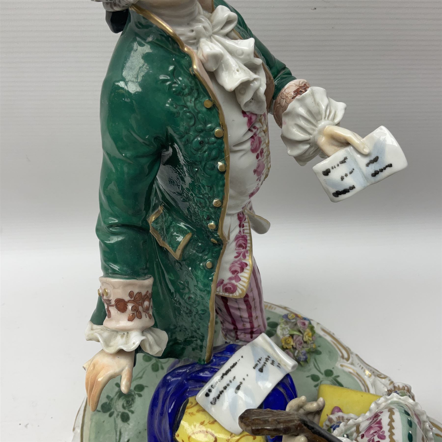 20th century Naples figure group, modelled as a seated female figure playing the lute seated, before a male figure stood holding a sheet of music, each in period dress, upon an oval base with gilt heightened scroll edge, with crowned N mark beneath, H31.5cm L33cm
