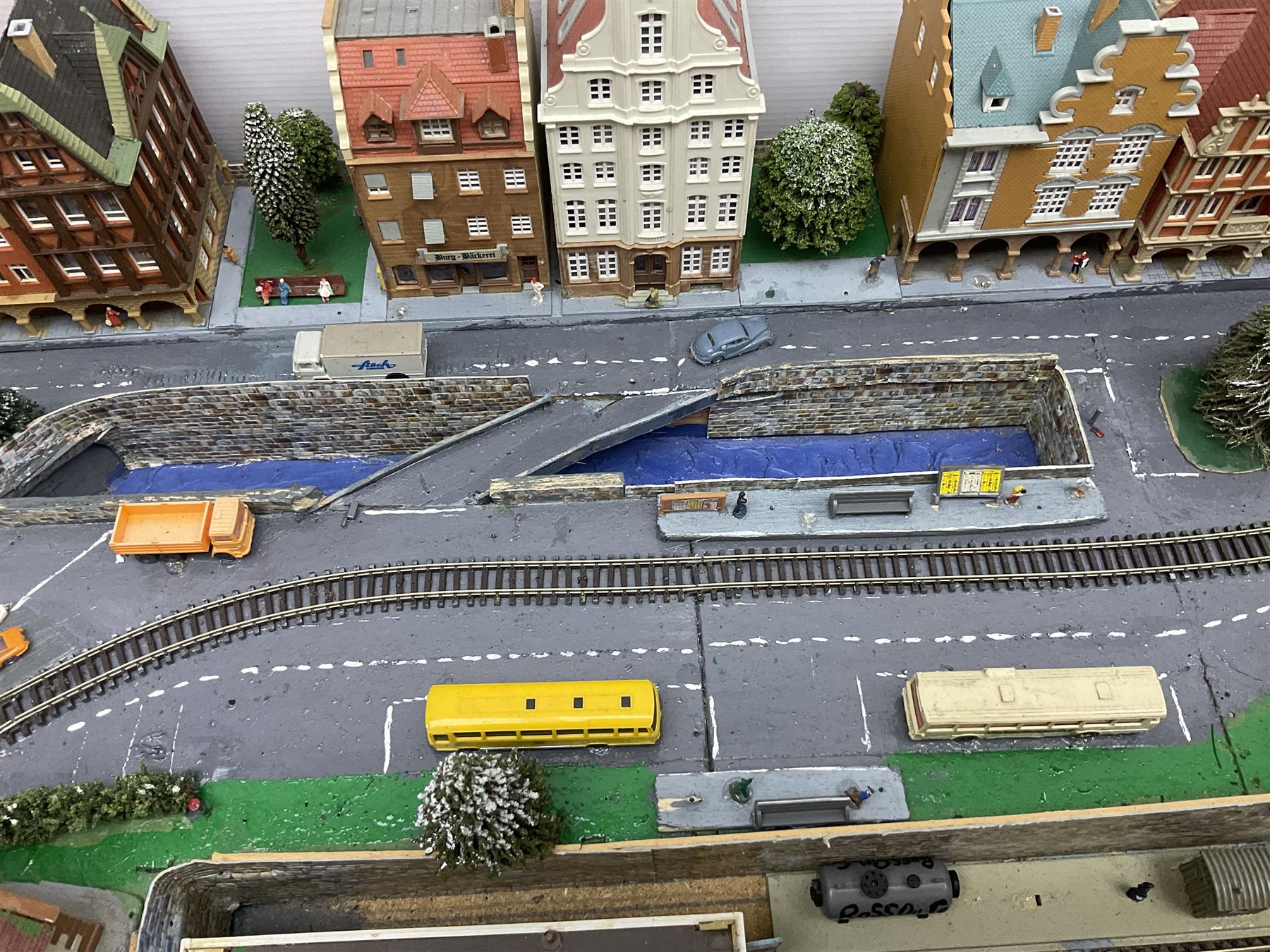 Table top 'N' gauge continental scenic layout as a split level town with various loops of track, station with numerous platforms, engine shed, assorted buildings, roads with motor vehicles and figures, tunnels, trees, river with bridge, tram depot etc 122 x 52cm