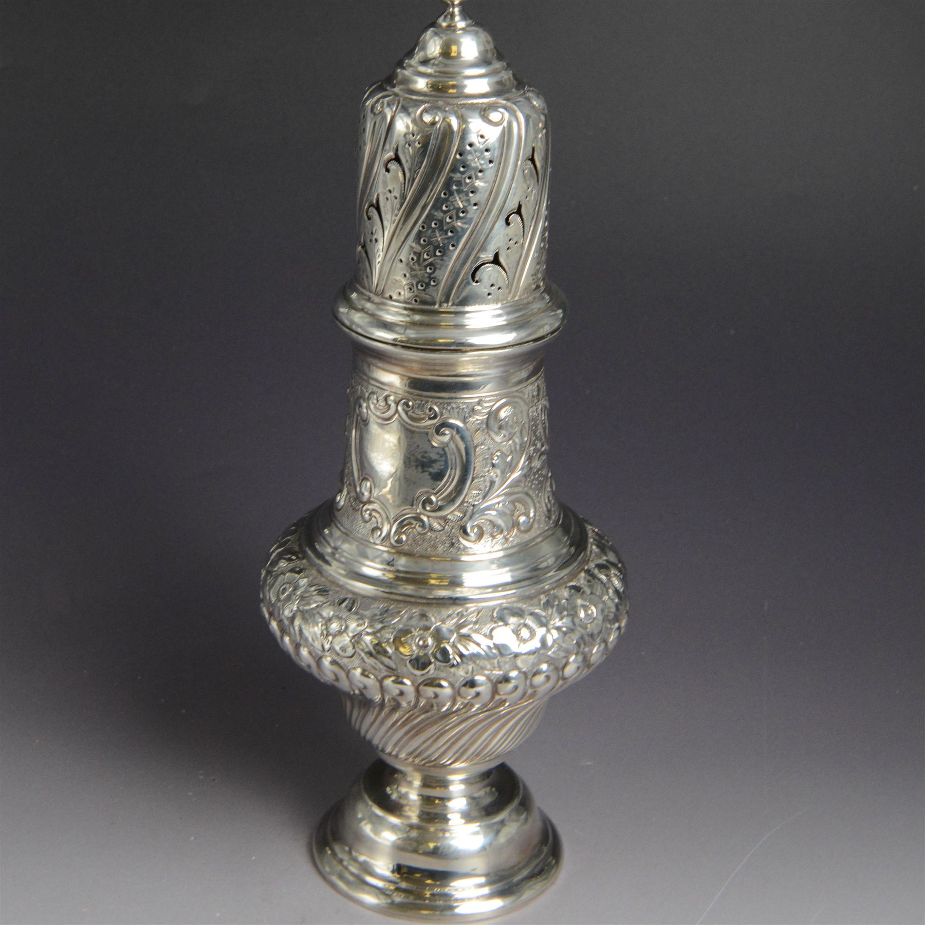 Victorian silver sugar caster, of bellied urn form, embossed with floral and foliate motifs, with two vacant cartouche, upon a domed stepped circular foot, with pierced removable cover with flambe finial, hallmarked Marston & Bayliss, Chester 1900, H25cm