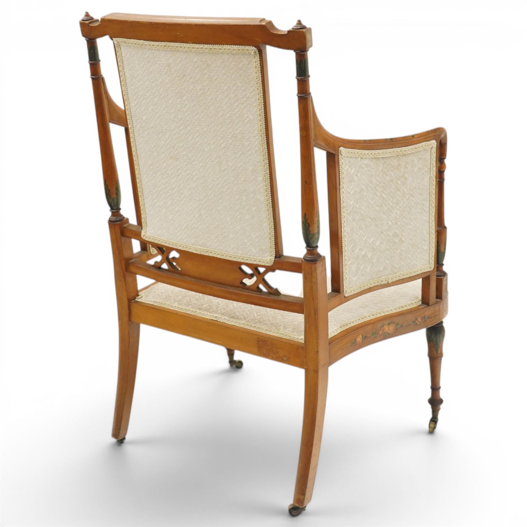 Pair of Victorian Sheraton Revival painted satinwood armchairs, the cresting rail painted with trailing floral bouquets flanked by illusion arcade motifs, over a cameo back and sides with acanthus painted swell-turned uprights, the lower back rail decorated with a bird scene and flanking pierced foliate design, upholstered in ivory fabric, raised on turned supports with further acanthus leaf paintwork, terminating to brass castors