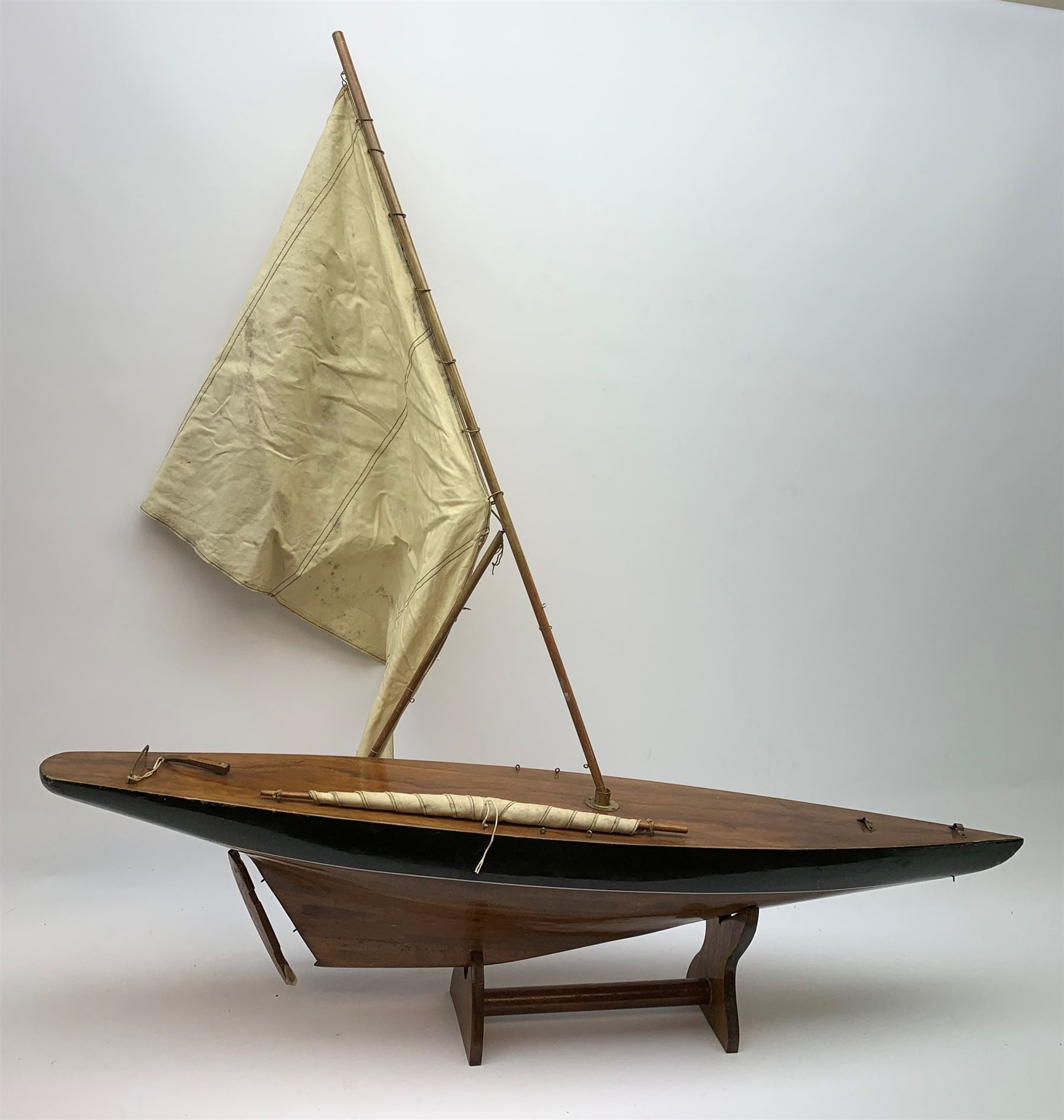 Pond yacht with part black painted mahogany hull and keel, working rudder and mast with three sails W90cm H95cm, loose mounted on mahogany stand
