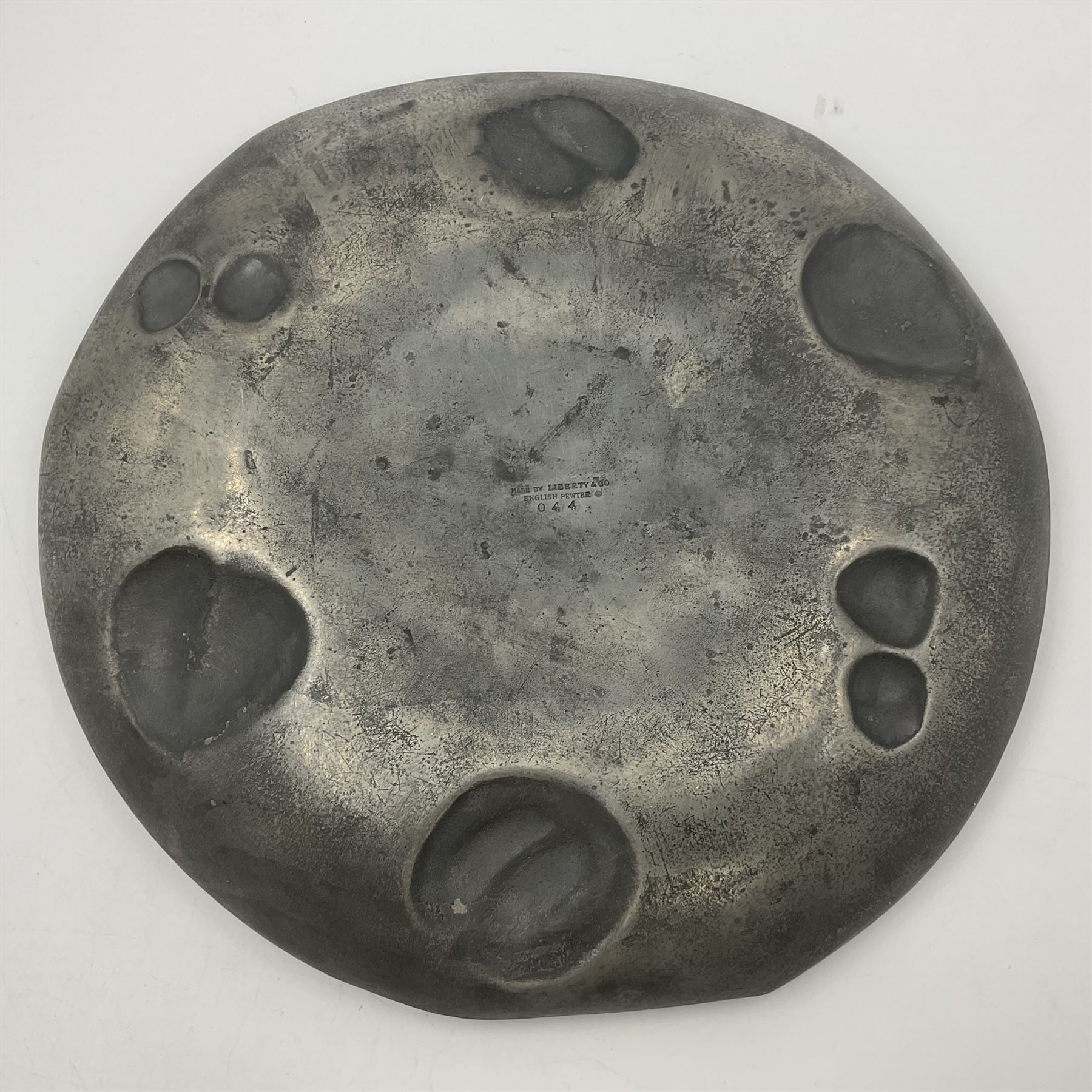 Liberty & Co Tudric pewter Bollelin tray, designed by Archibald Knox, of circular form with shaped edge, cast in relief with foliate tendrils surrounding a green enamel cartouche, impressed beneath Made by Library & Co English Pewter 044, D25.5cm