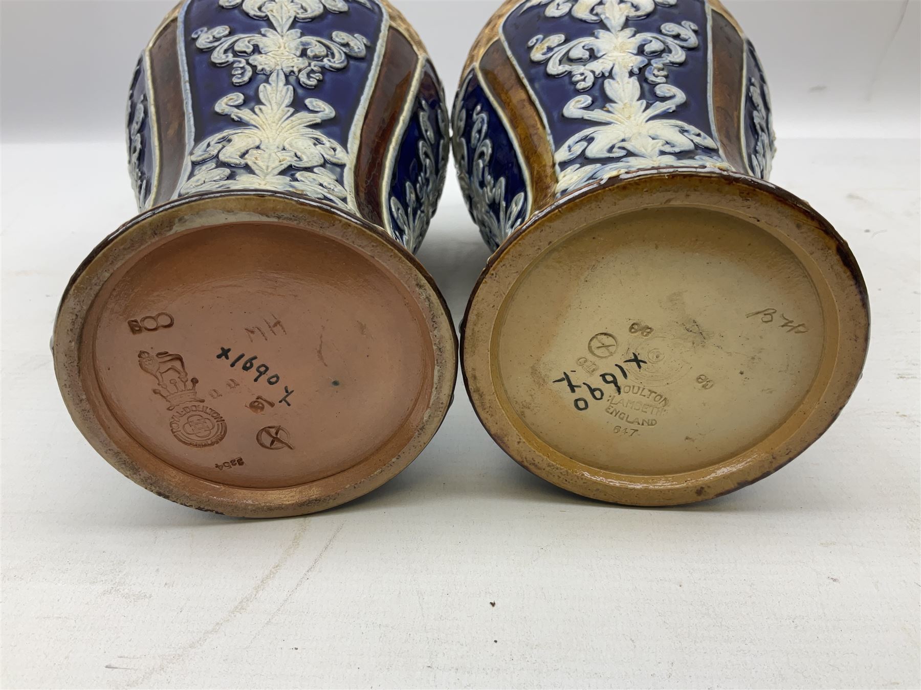 Pair of Royal Doulton Lambeth stoneware baluster vases, decorated in light relief with panels of foliage on blue ground, with gilt scrolls above, impressed mark beneath, 28cm high