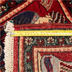 Two small rugs, an ivory ground example decorated with a central floral medallion and scattered rose sprays, enclosed by a navy foliate border (62cm x 101cm), and a crimson pictorial mat worked with seated figures, an animal and birds amongst flowering plants (45cm x 79cm) (2)