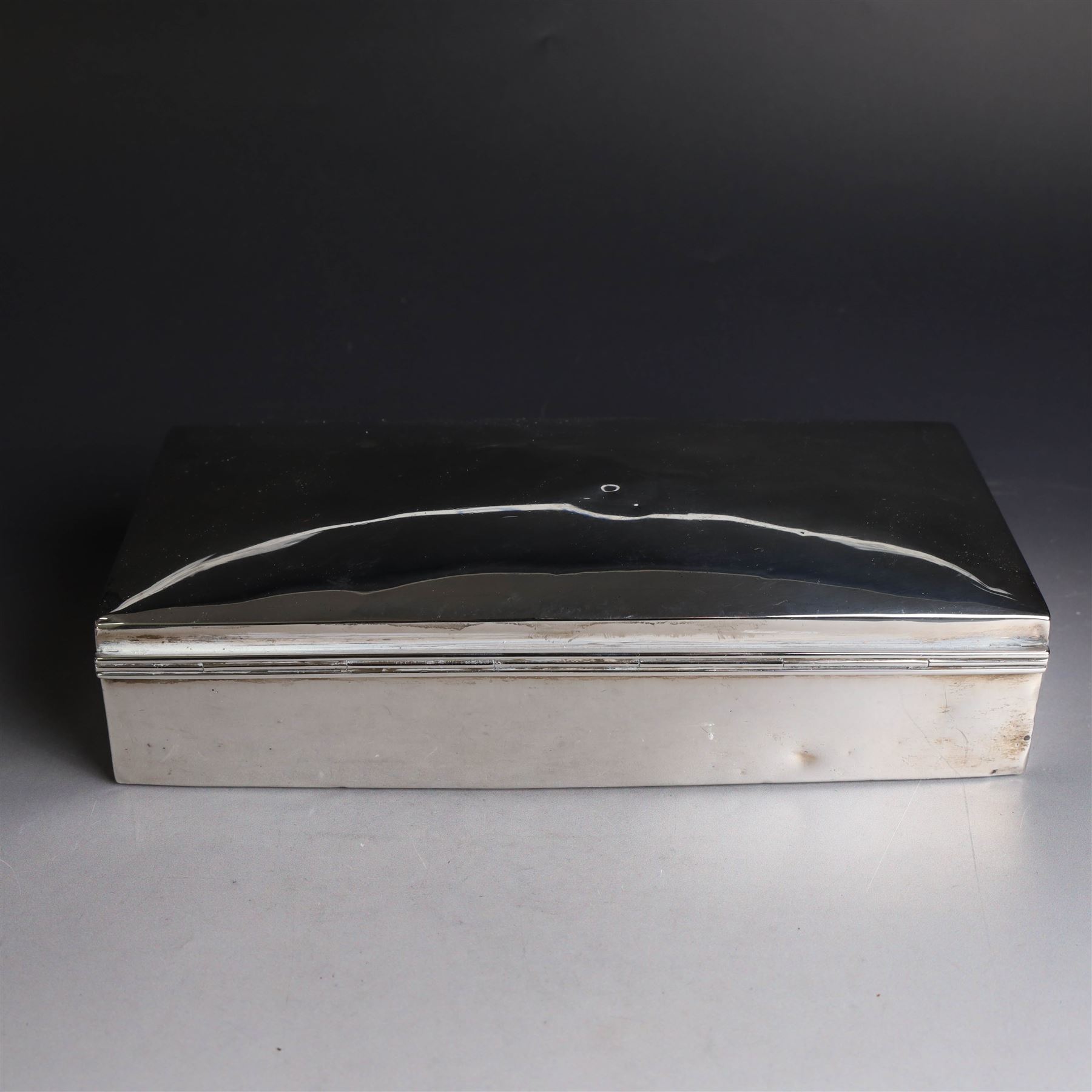 Two silver cigarette boxes, comprising early 20th century plain rectangular example with compartmentalised softwood interior, hallmarked Birmingham 1914, maker's mark indistinct, and an early 20th century example with engine turned decoration and engraved initials to cover, hallmarks worn and indistinct, largest H4.5cm, W21cm