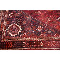 Large Persian Shiraz crimson ground carpet, the busy field decorated with a geometric pole medallion surrounded by stylised plant motifs with contrasting indigo spandrels and geometric-woven guard bands