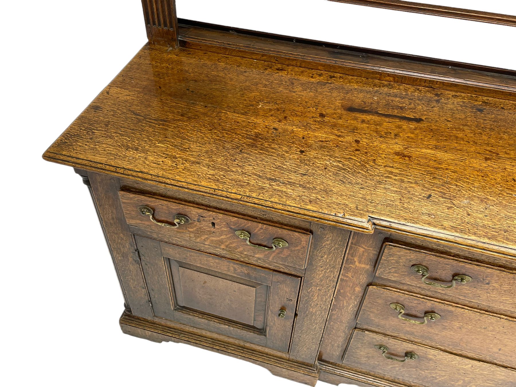 George III oak dresser, projecting dentil cornice over three heights plate rack enclosed by fluted uprights, the dresser fitted with five drawers and two panelled cupboards, canted corners with fluted quarter columns, on bracket feet