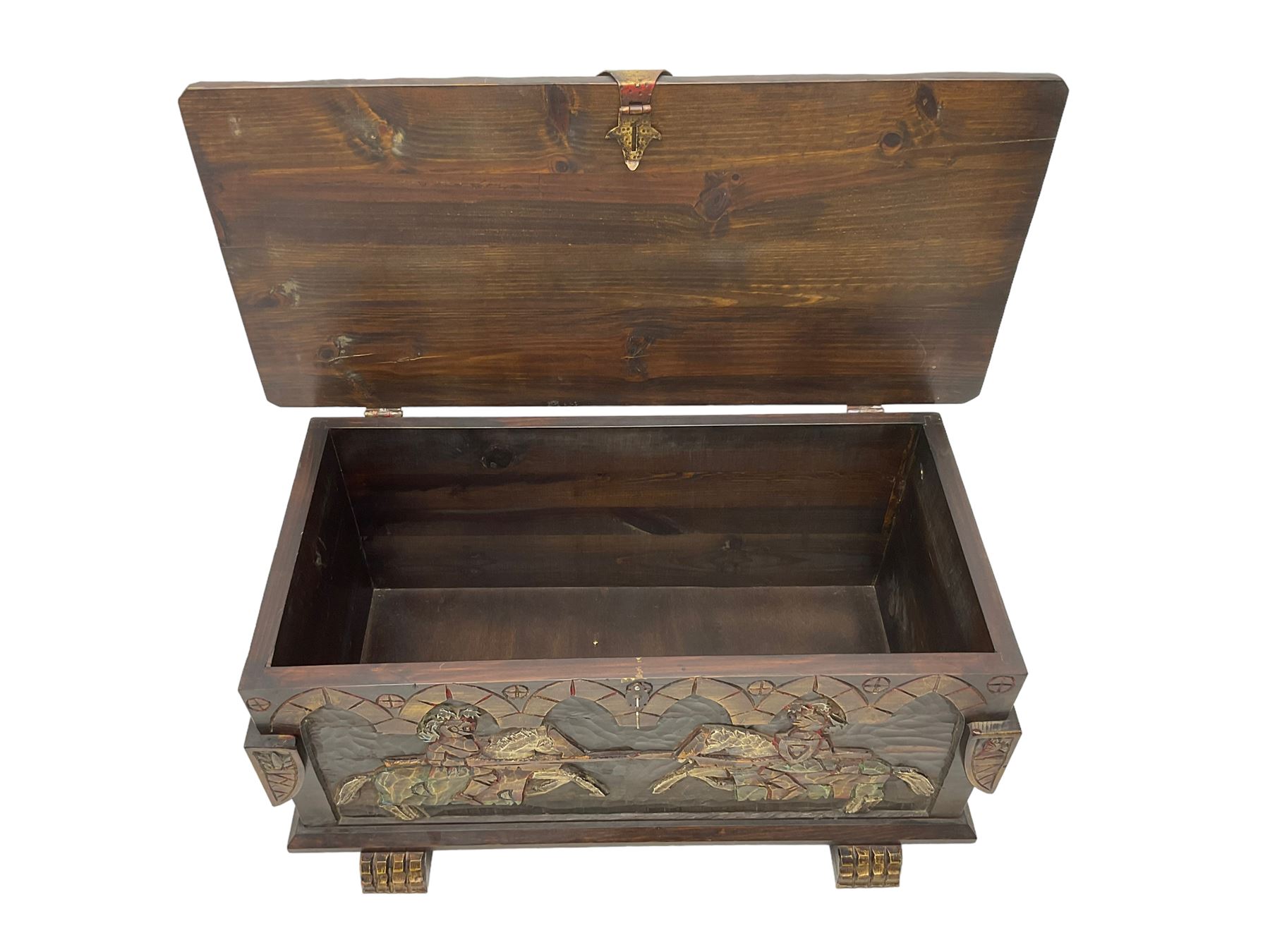 Carved wooden blanket chest, the tooled hinged lid with shaped metal strap hinges and catch, the front carved with arcade over two medieval jousters, on carved sledge feet