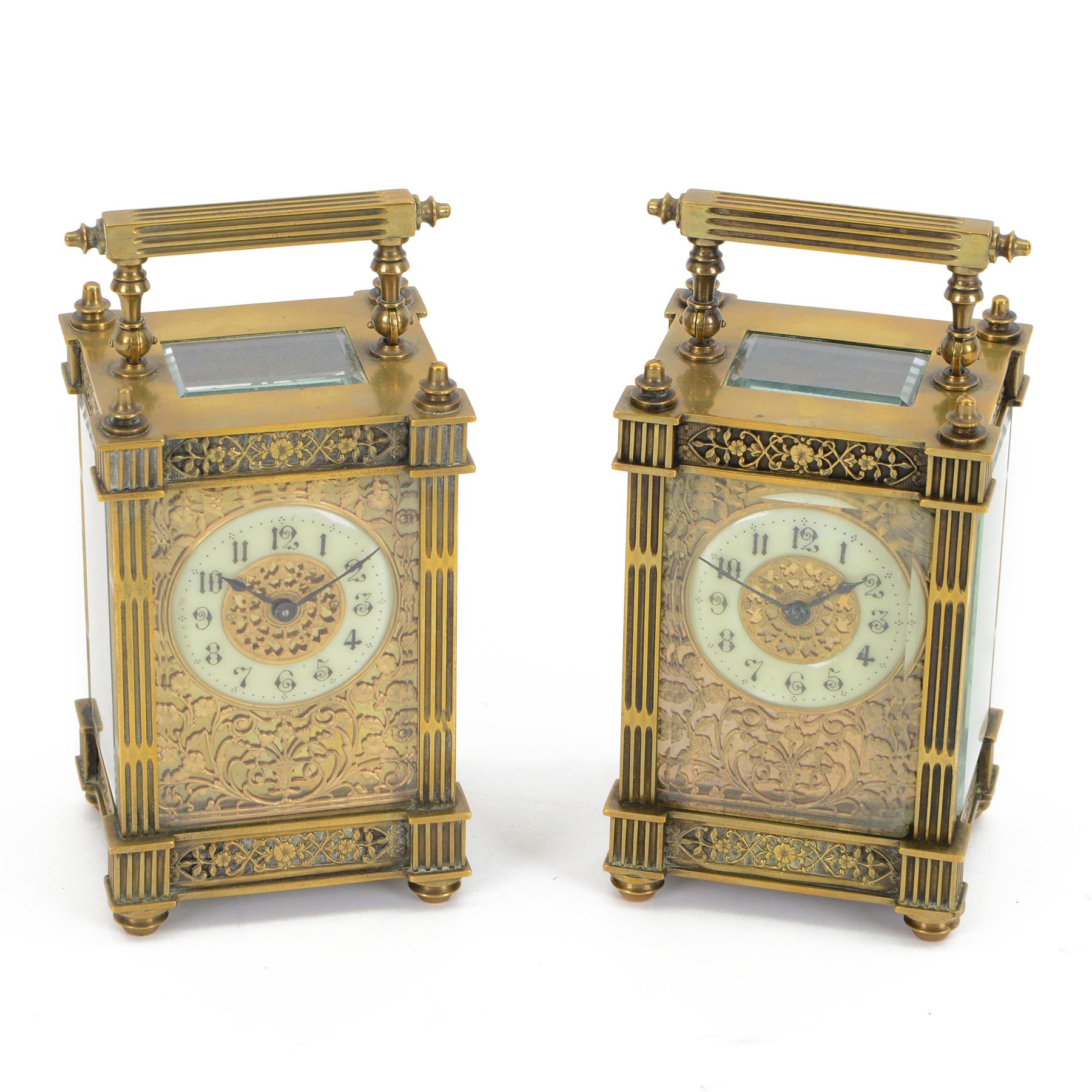French - Matching pair of Edwardian 8-day timepiece carriage clocks with bevelled rectangular glass panels and overlaid friezes in gilt repousse work with fretted dial masks,  circular enamel chapter ring with Arabic numerals and steel spade hands, both clocks with single train movements, one movement with a jewelled cylinder platform escapement and the other with a jewelled and silvered lever platform escapement.
No Keys.