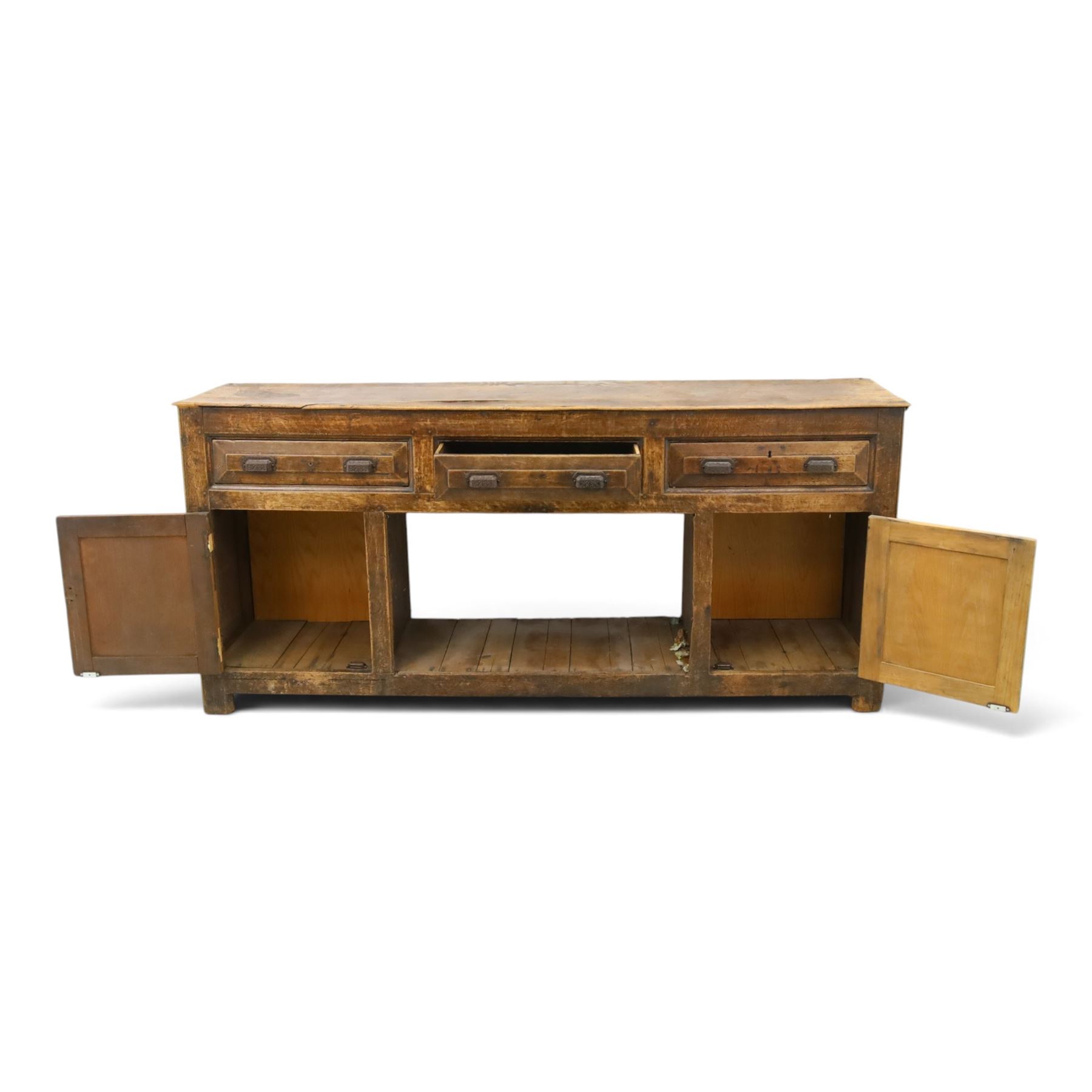 18th century rustic oak dresser base, with fielded panels and iron cup handles with embossed greek key and foliate detail, three short drawers above and open recess flanked by two cupboard doors, raised on stile supports