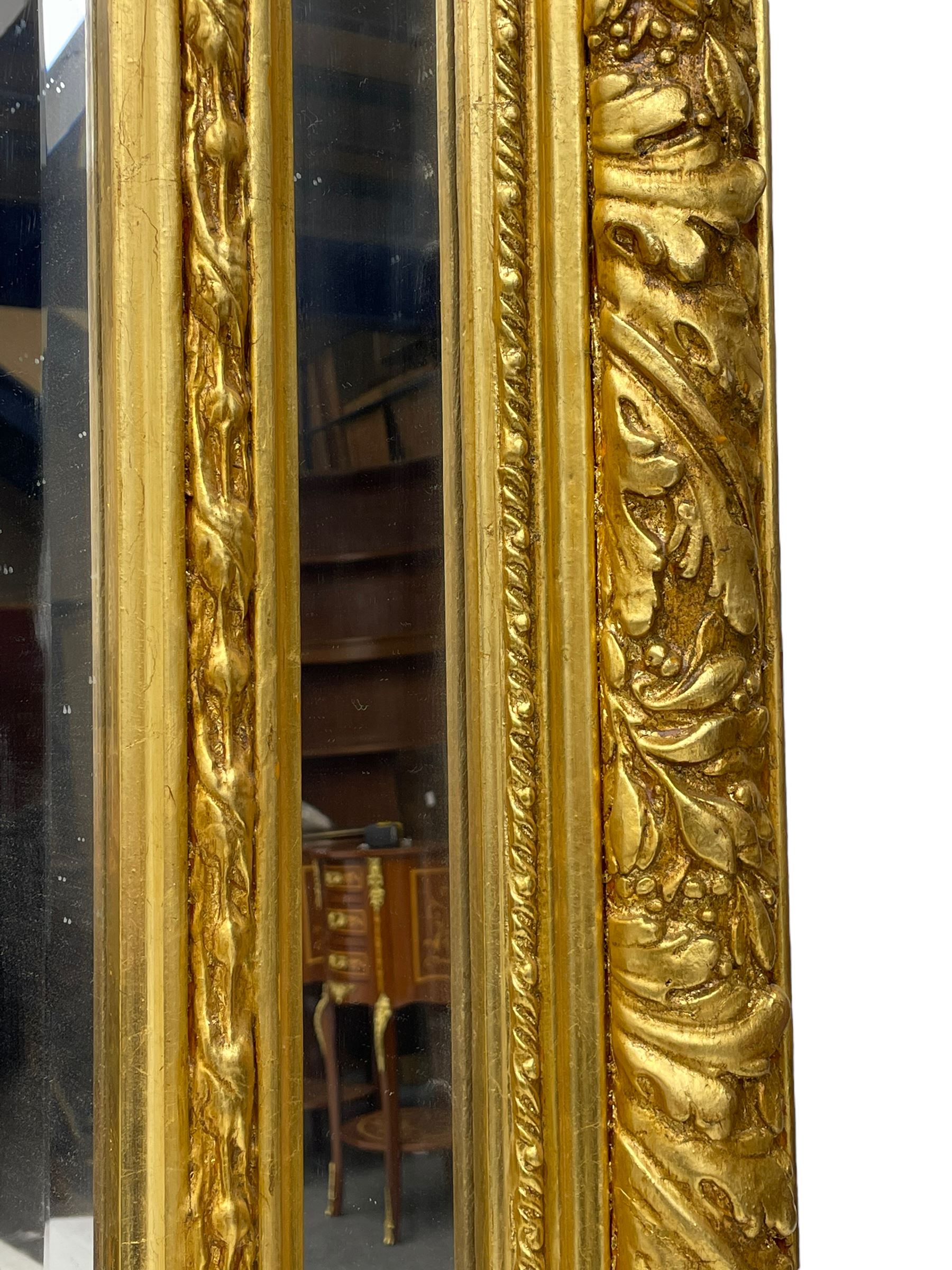 Large Italian Baroque design gilt wall mirror, the shell pediment over circular panel depicting classical female flute player with dancing putto within a tree landscape, the stepped arched upper frame surmounted by musical instrument playing putto and trailing flower heads, central bevelled mirror plate surrounded by plain segmented mirror plates, acanthus leaf moulded outer frame and foliate moulded inner slip