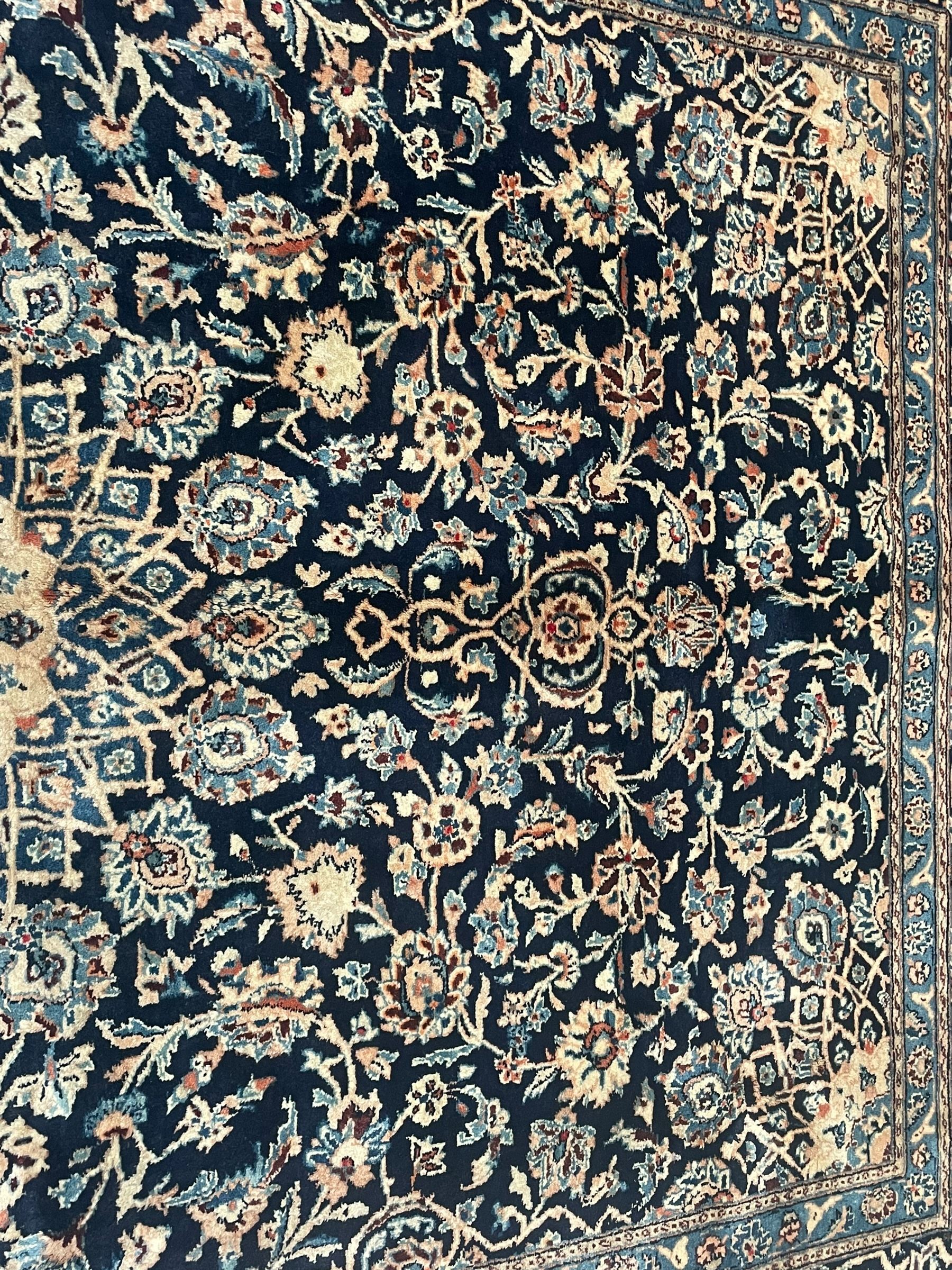 Persian Kashan indigo ground rug, the rosette medallion decorated with projecting palmettes, on a field of swirling leafy branches and decorated with further palmettes, the scrolling border with repeating stylised plant motifs, within floral pattern guard stripes