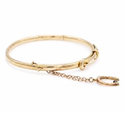 Early 20th century 15ct gold buckle hinged bangle, stamped 15, the safety chain with a 9ct rose gold horseshoe charm, set with a single sapphire