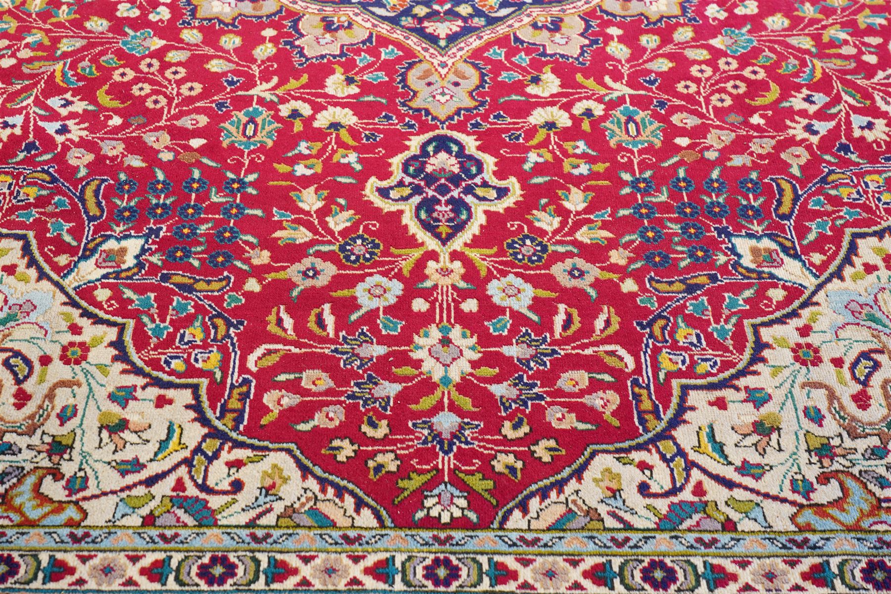 North West Persian Tabriz hand-knotted carpet, madder red field with a central cusped medallion issuing radiating pendants and an all-over design of scrolling arabesques, palmettes and flowering vinery enclosed by conforming spandrels, indigo main border of meandering floral vines and stylized palmettes, flanked by narrow guard stripes, cotton fringe ends 