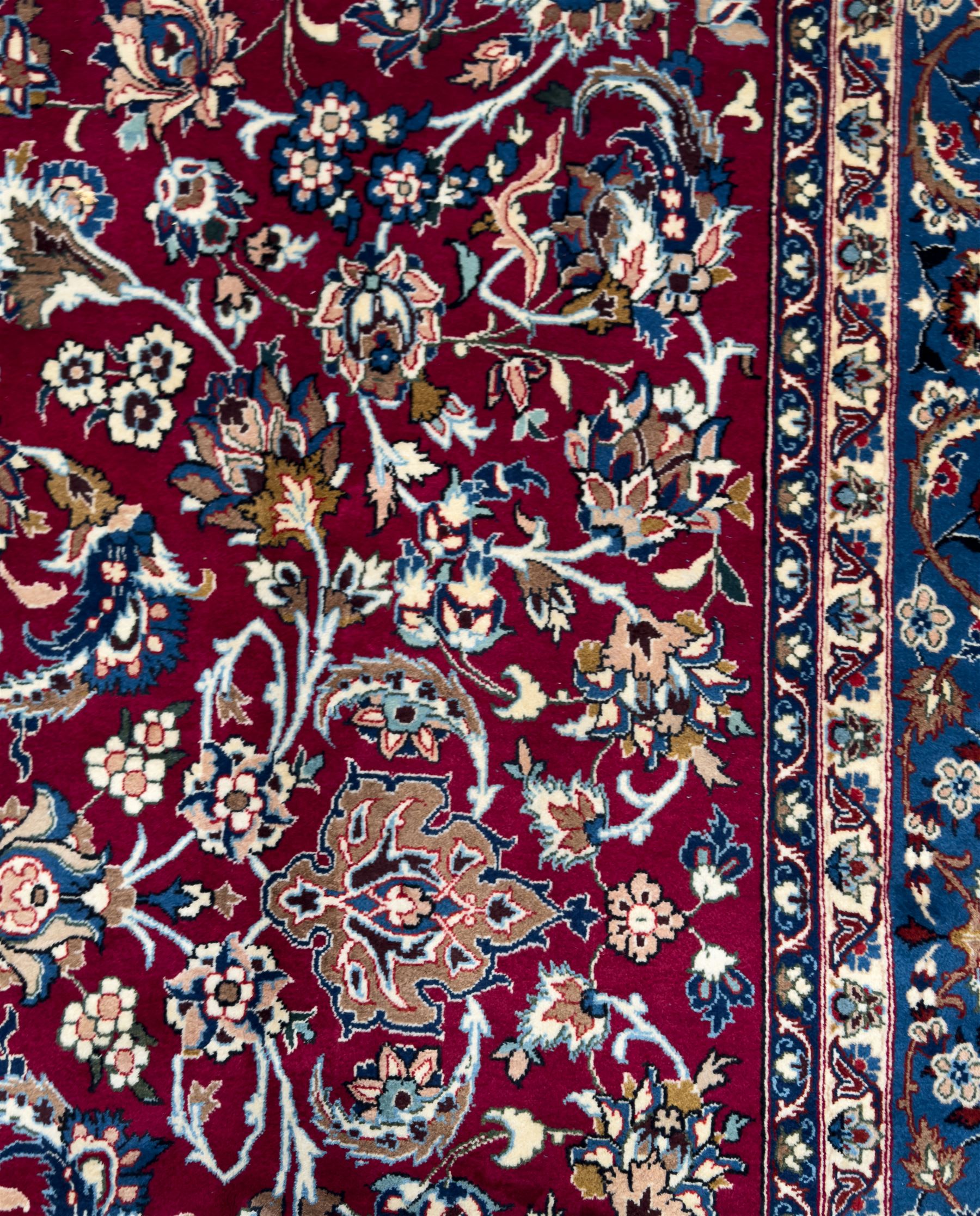 Central Persian Yazd hand-knotted rug, madder red field with scrolling vines, palmettes, and rosettes around a cusped lozenge medallion within a blue ground border of palmettes and flowerheads, 366cm x 250cm
