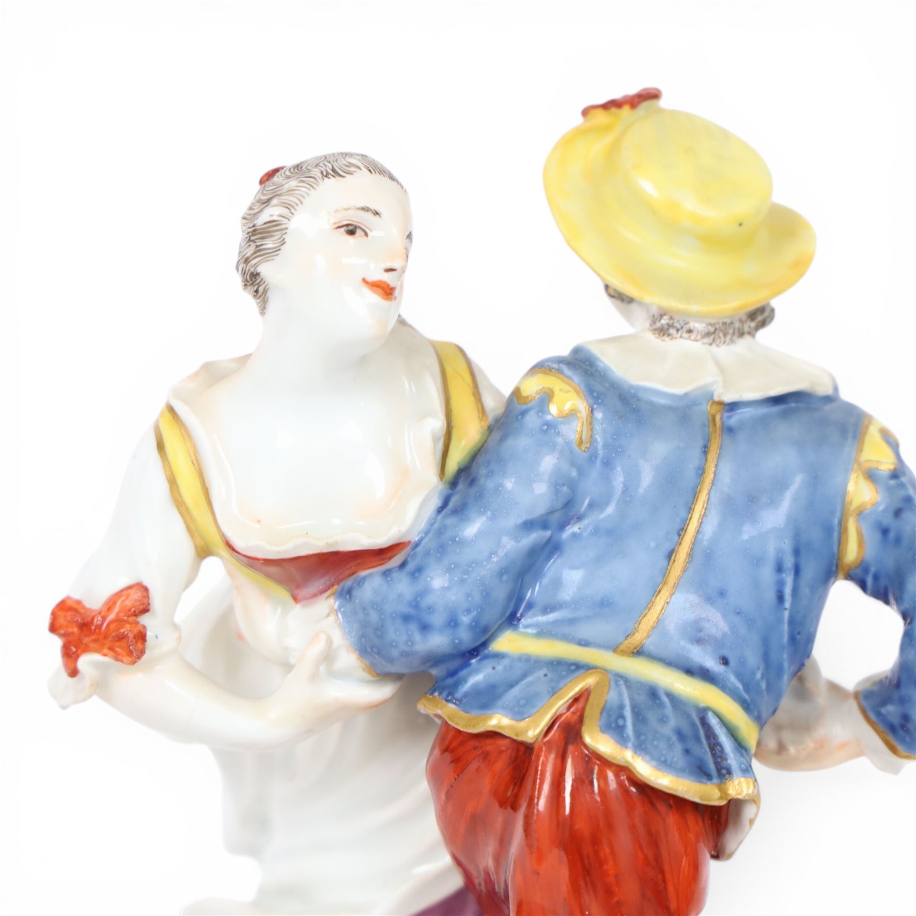 Mid 18th century Meissen figure group, The Tyrolean Dancers, circa 1740, modelled as two swirling figures with their arms linked, he in yellow hat with red rosette, blue jacket, red breeches with red rosette, and yellow shoes with green rosette, she in white blouse with red ribbons, yellow and red bodice, white apron over puce skirt and yellow shoes with green rosettes, her hair fashioned into two plaits secured by red ribbon, upon a shaped mound base, within a scrolling gilt metal mount, with blue crossed swords mark to base, overall H19cm
