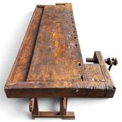 Large early 20th century rustic stained reclaimed pine workbench, the substantial plank top with recessed tool well and two homemade wooden screw vices, above a single frieze drawer and slatted undertier, raised on trestle end supports
