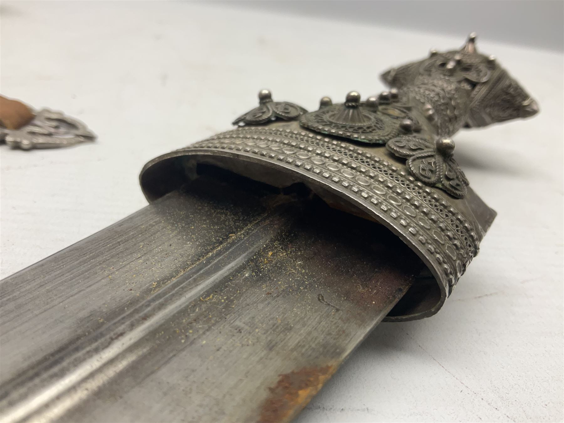 Omani Khanjar dagger, the 19cm curved blade with pronounced medial rib to either side, waisted hilt with dome shaped pommel and silver covered horn grip decorated with filigree bands, floral motifs and beadwork; in an intricately filigree decorated silver and leather scabbard with silver rings woven into the belt mount and fitted with original silver thread-work belt L34cm overall belt length 94cm