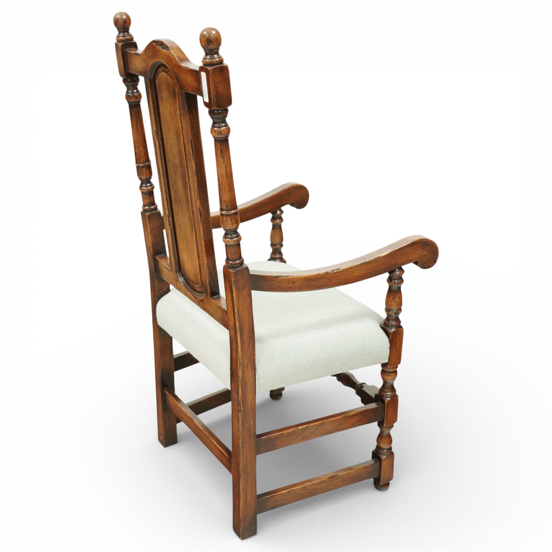 Country House oak high back dining chairs, set of ten comprising eight side chairs and two carvers, each with arched top rail flanked by turned finials over a central fielded panel back, with overstuffed seats upholstered in pale fabric, raised on turned front supports united by stretchers