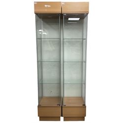 Pair light oak and glass single display cabinets, glazed back and sides with single glazed door enclosing three shelves, light fitting to top