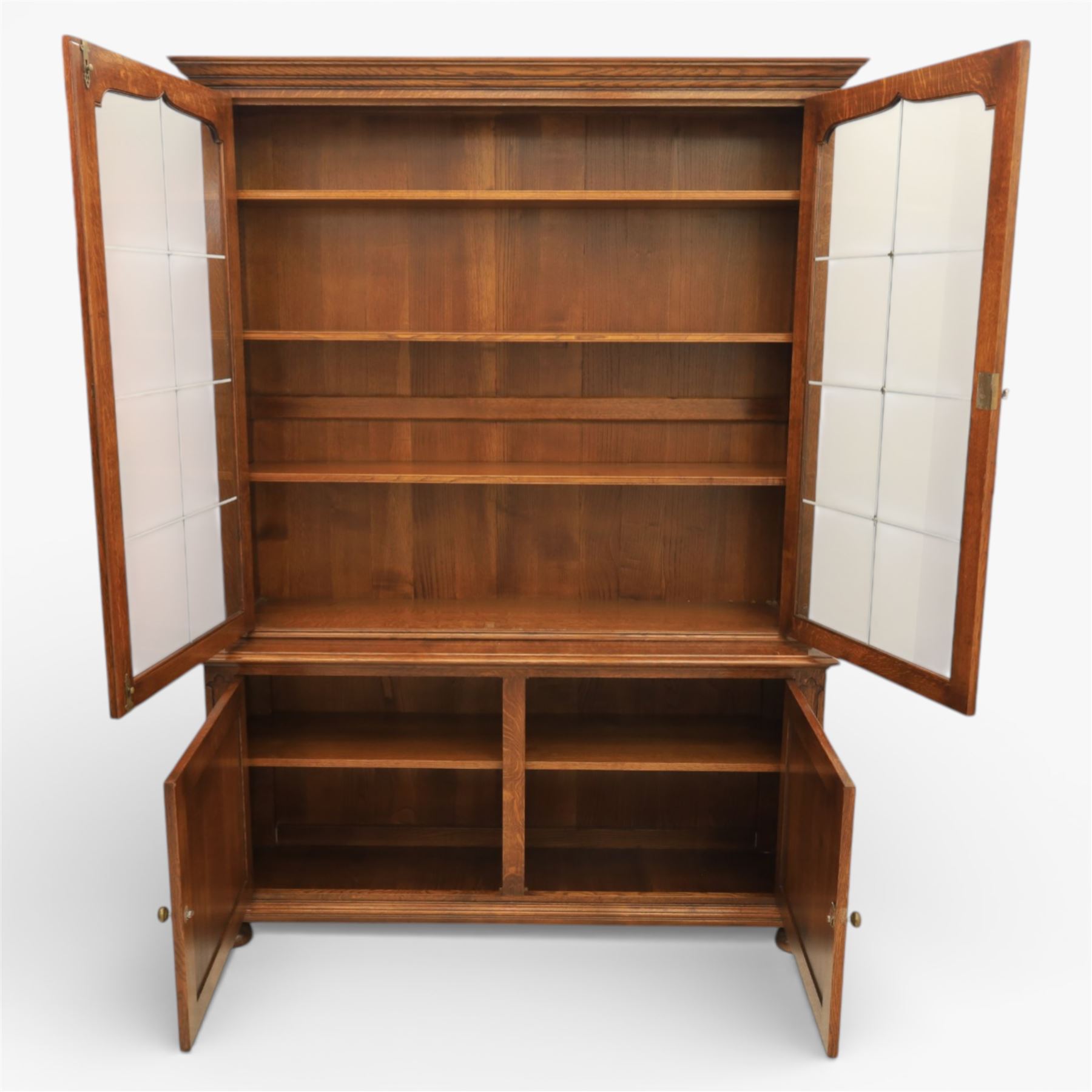 Late 20th century oak bookcase on cupboard, with moulded cornice above pair of astragal glazed doors with shaped inner frames enclosing adjustable shelves, the base with moulded top above two fielded panel cupboard doors with brass handles, upon compressed bun front feet 