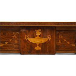 Edwardian Sheraton Revival inlaid plum pudding mahogany serpentine sideboard, rectangular top with raised gallery above bowed frieze drawer finely inlaid with central neoclassical urn motif, flanked by two drawers with swags and ribbon bows, above a cellarette drawer and cupboard, on square tapered supports with spade feet 
