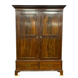 George III mahogany double wardrobe, the projecting cornice with dentil moulding over two panelled doors with mirror-lined interiors, enclosing hanging rails and brass hooks, the base fitted with two drawers, raised on bracket feet