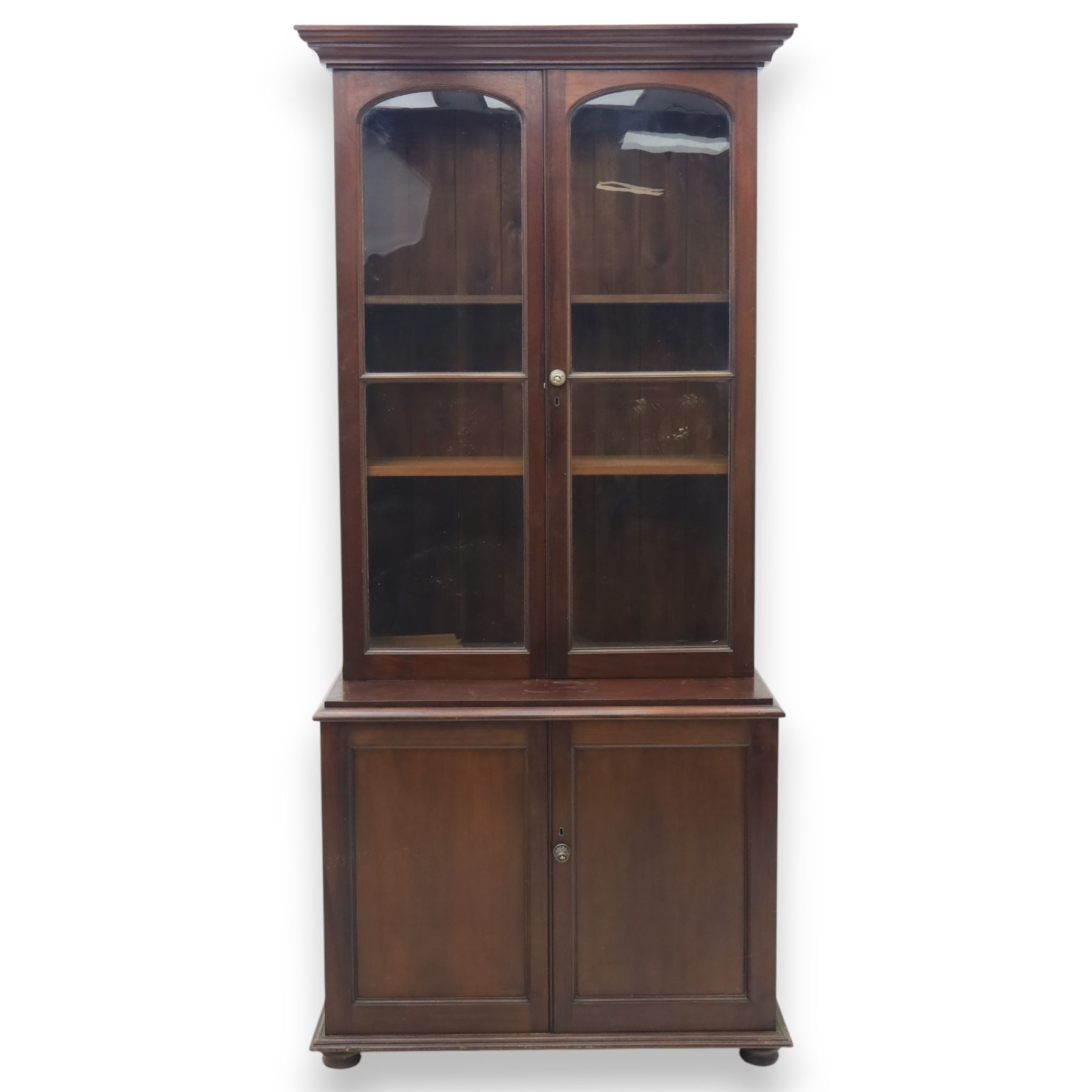 20th century mahogany display bookcase, projecting moulded cornice over a pair of glazed doors with shaped upper glazing and plain lower panes, opening to reveal shelved interior, the base with two recessed panel cupboard doors, raised on a moulded plinth with compressed bun feet