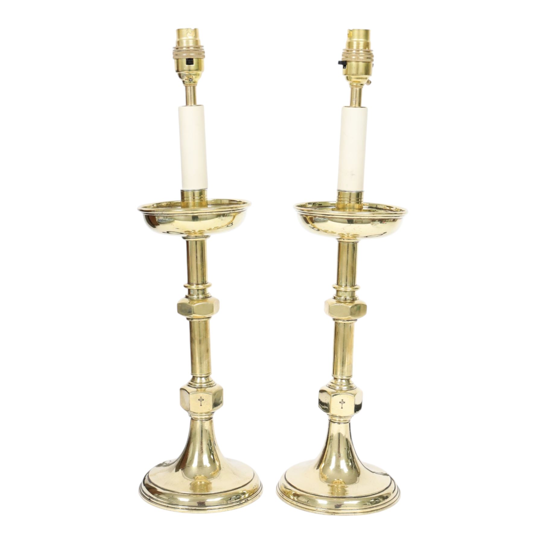 Pair of early 20th century brass alter candlesticks converted to table lamps, each with stepped and spreading circular base leading to a double hexagonal knopped column, and plain socket above inverted domed circular drip pan, the socket with light fitting, overall H49cm