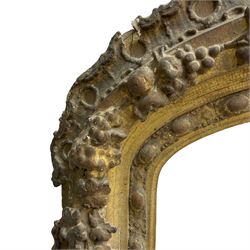 19th century giltwood and gesso moulded picture or mirror frame, the arched cresting rail mounted by central cartouche decorated with foliate scrolls and fruit, the outer frame decorated with scalloped edge and shell mouldings, trailing foliage with flower head and fruit to the central band, egg and dart moulded inner slip
