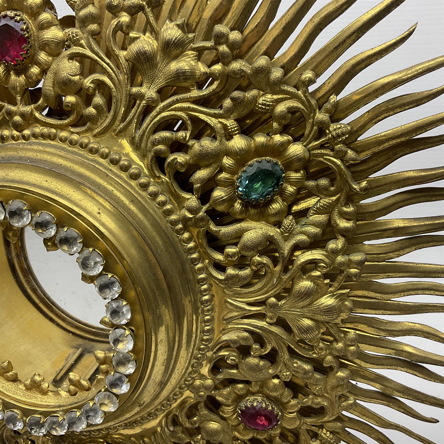 20th century gilt metal monstrance, in the Gothic revival style, with glazed aperture to centre surrounded with clear paste stones, in a pierced floral and scroll border set with coloured paste stones, within a sunburst surround, on a paste set knopped stem and similar foliate foot, H59.3cm
