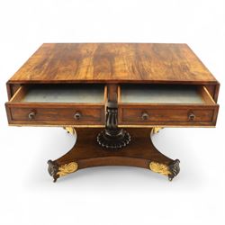 Regency rosewood sofa table, rectangular top with variegated rosewood veneers, hinged D-shaped leaves, over a set of dummy drawers to the back and full-size drawers to the front, with turned knob handles and gilt beaded moulding on frieze above elegant turned, tapering, and fluted, pedestal with a well-carved collar, supported on a large, tripartite concave platform base terminating in richly carved lion paw feet with gilded acanthus leaf carving, on concealed brass castors, circa 1815, length extended 161cm 
