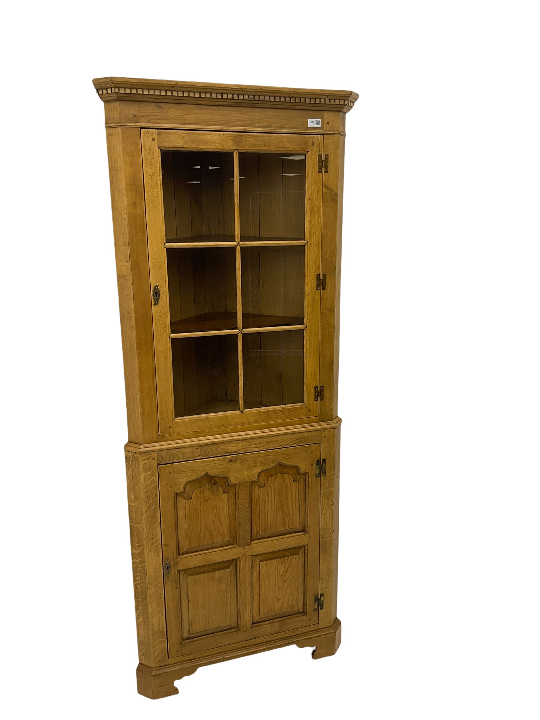 Traditional light oak corner cabinet, projecting cornice, dentil frieze, single glazed door above single fielded door