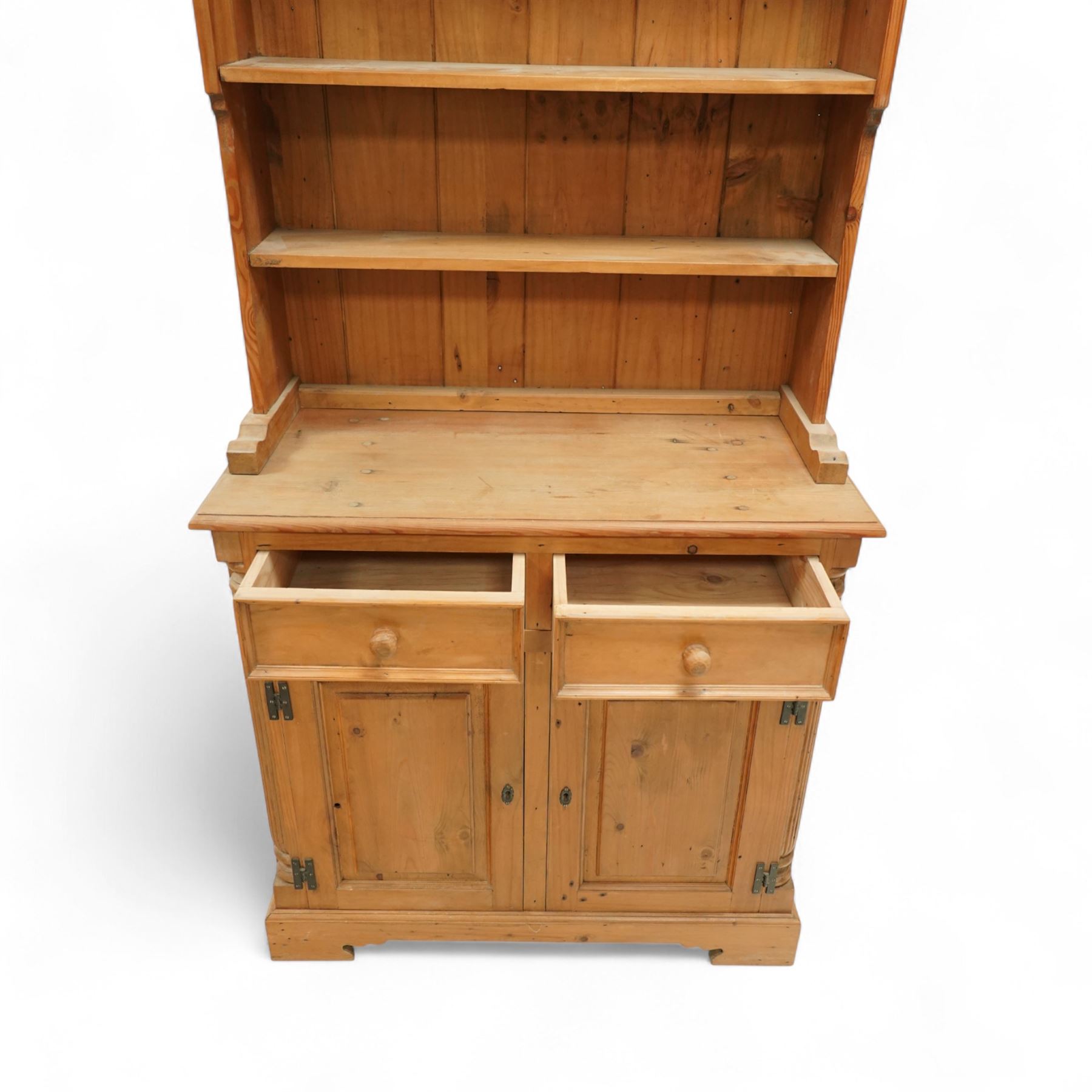 20th century stripped pine dresser, the open rack with dentil frieze and fixed shelves over a cupboard base with two drawers and fielded panel doors, flanked by stop-fluted uprights, on a moulded plinth