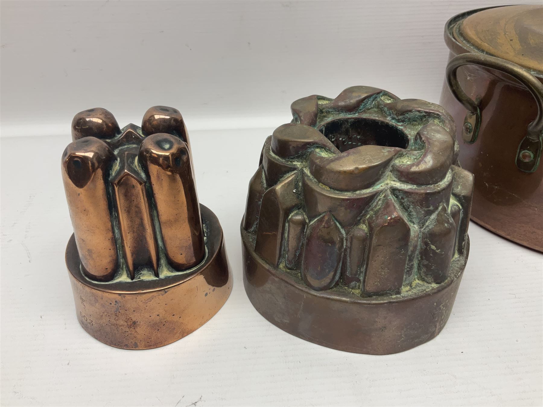 Four Victorian copper moulds, together with a graduating set of copper pans with wooden handles and finials to covers, largest pan 