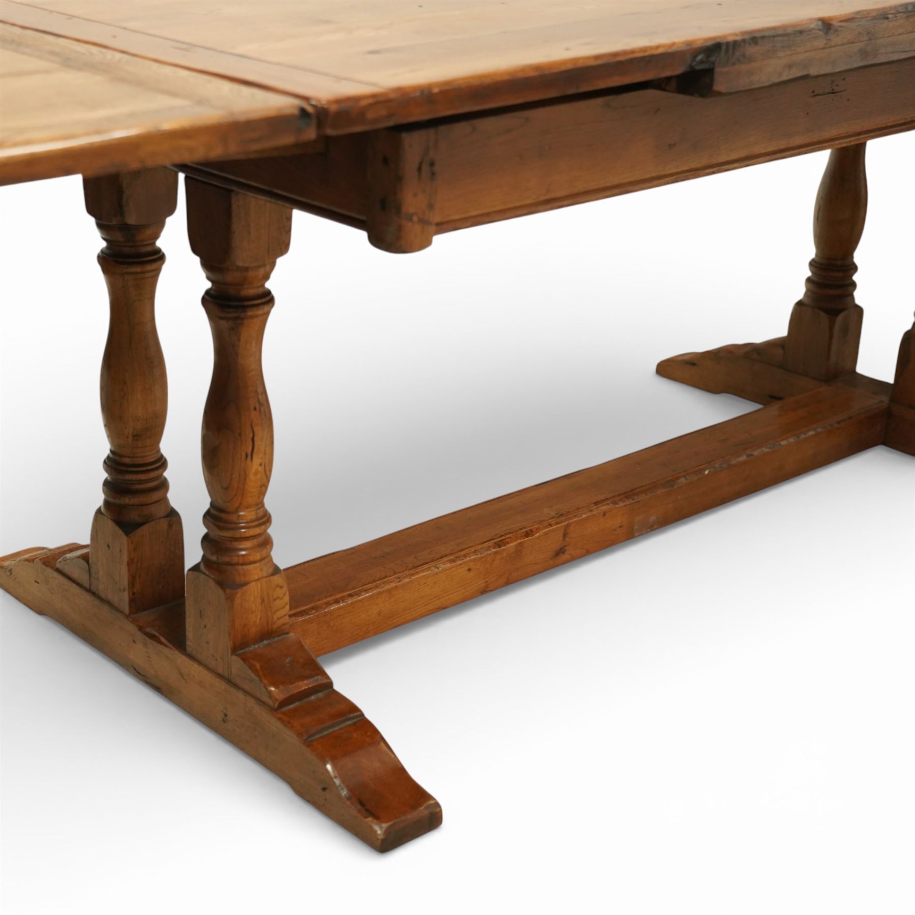 Late 20th century light oak extending refectory table, in the manner of Titchmarsh & Goodwin, rectangular plank top with cleated ends and two draw leaves extending to 260cm, supported on turned end supports united by a stretcher, raised on block feet