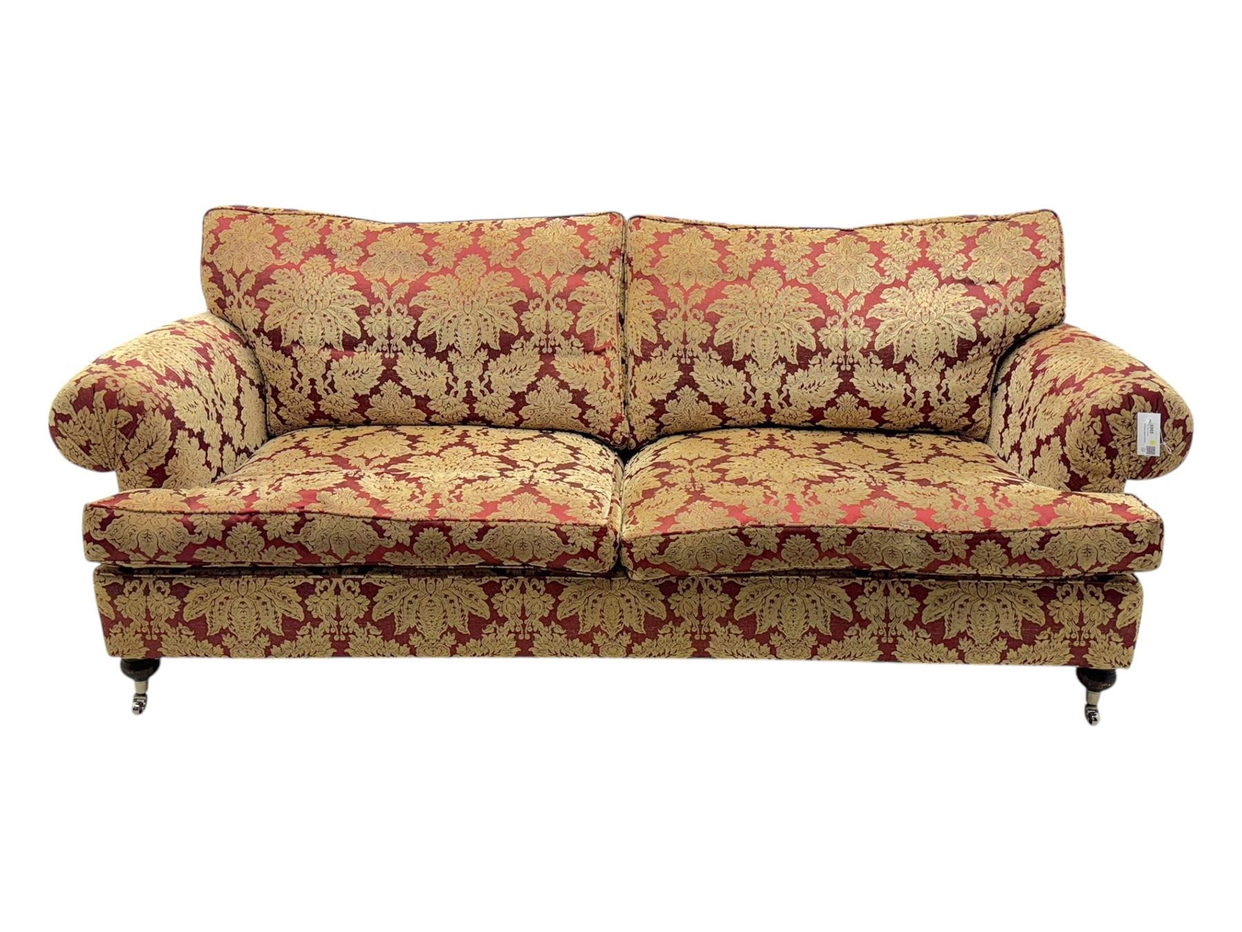 Duresta - pair of Grande three-seat sofas, traditional shaped with rolled arms and upholstered loose cushions, in red ground fabric with raised gold foliate pattern, on turned feet with brass castors 