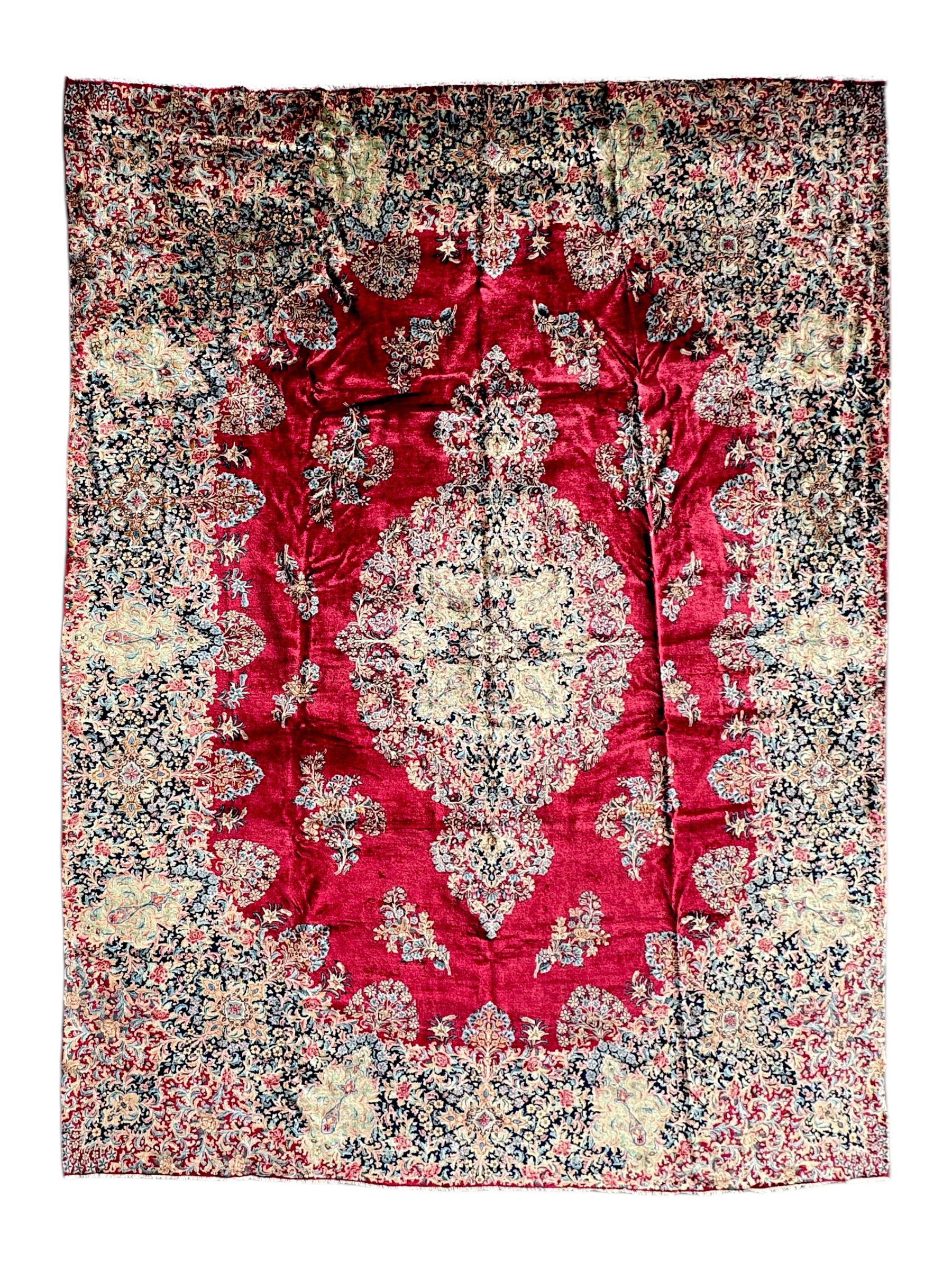 Persian Kirman carpet, the bold ruby field hosting a multi-lobed central medallion, embellished with scrolling vines and floral sprays, edged by layered borders and trimmed with short fringe